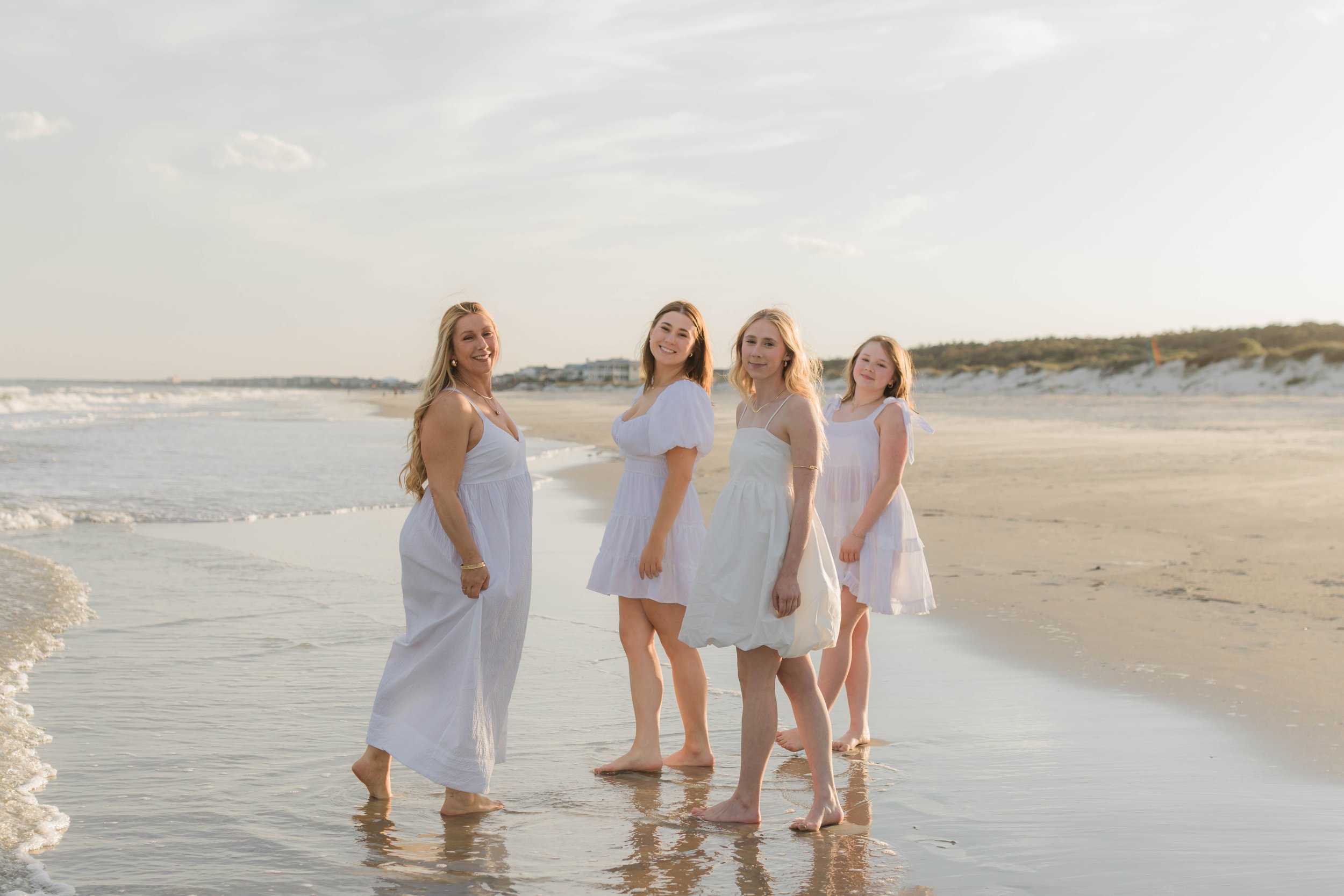Mother and three daughters smiling and walking barefoot along the shoreline at sunset, Huntington Beach State Park