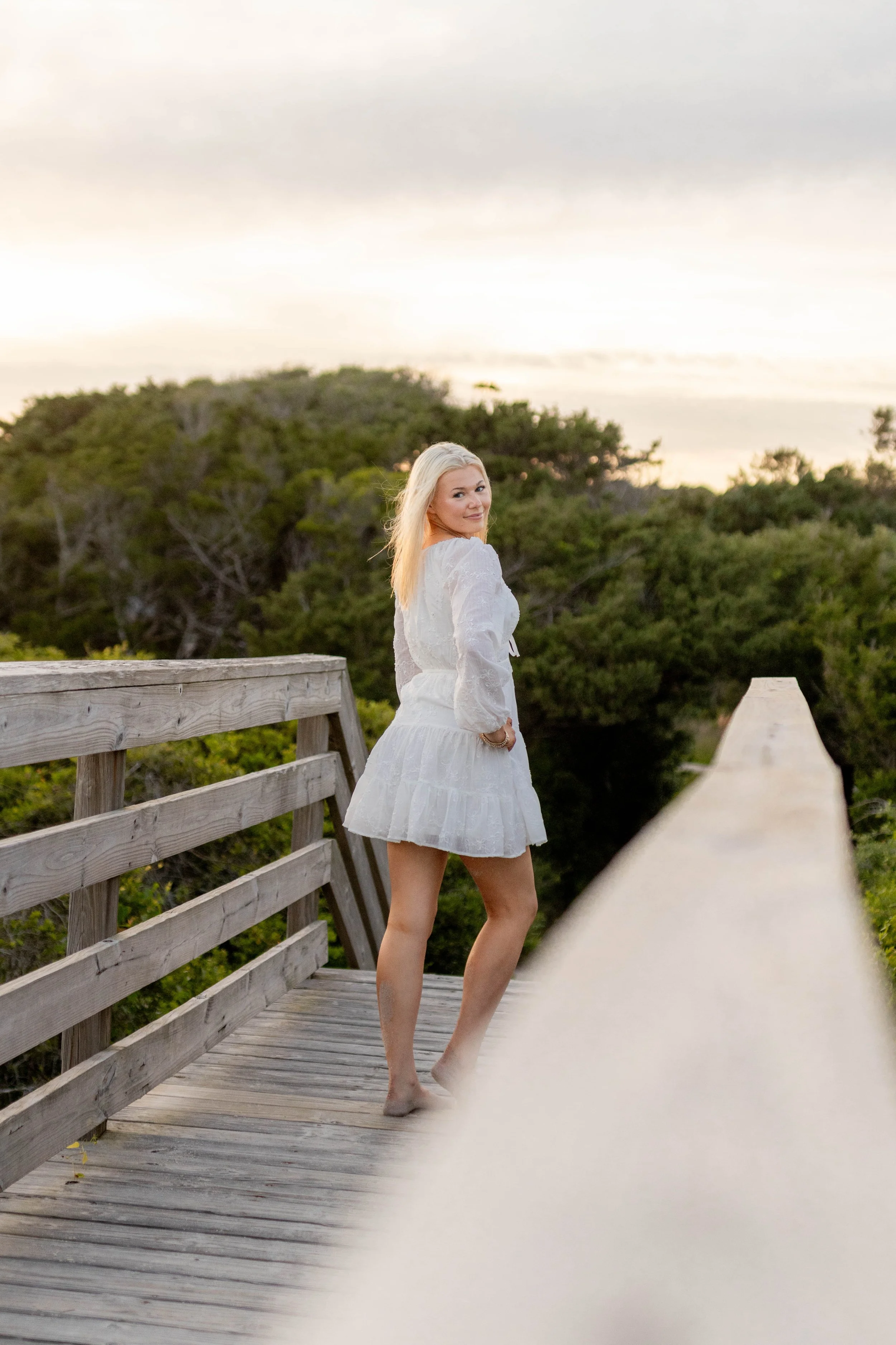 High school senior in Myrtle Beach wearing cap and gown during golden hour beach photo session, splashing in the water and smiling, taken by Myrtle Beach family and senior photographer.