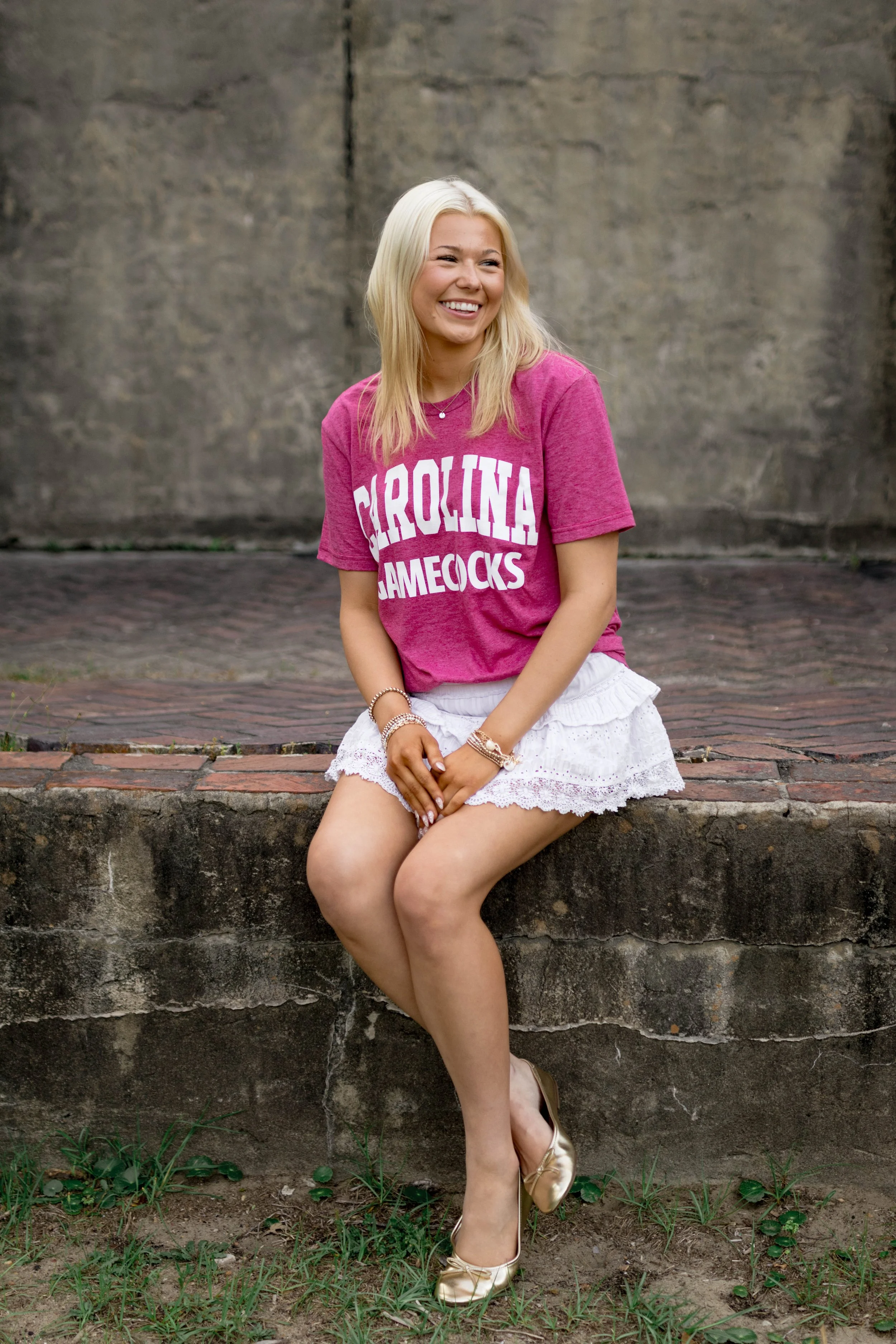 High school senior in Myrtle Beach wearing cap and gown during golden hour beach photo session, splashing in the water and smiling, taken by Myrtle Beach family and senior photographer.
