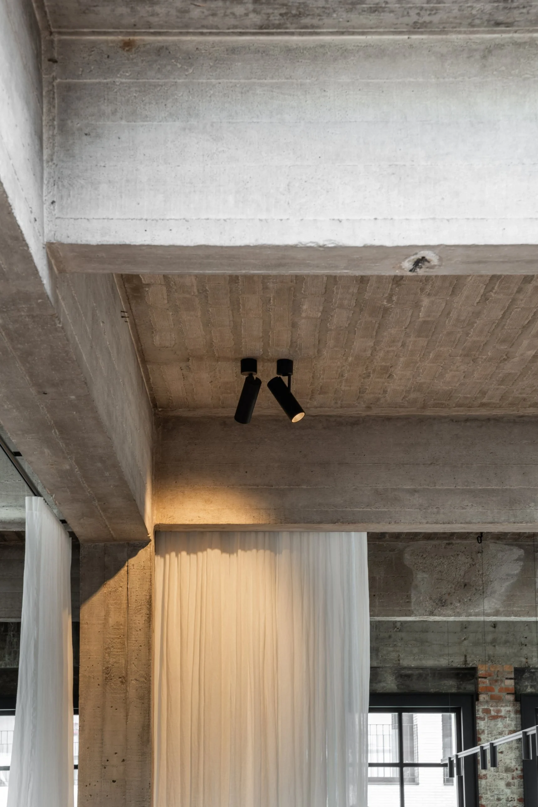 Black Kreon Holon 60 Directional Surface spotlights washing a linen curtain between raw concrete beams
