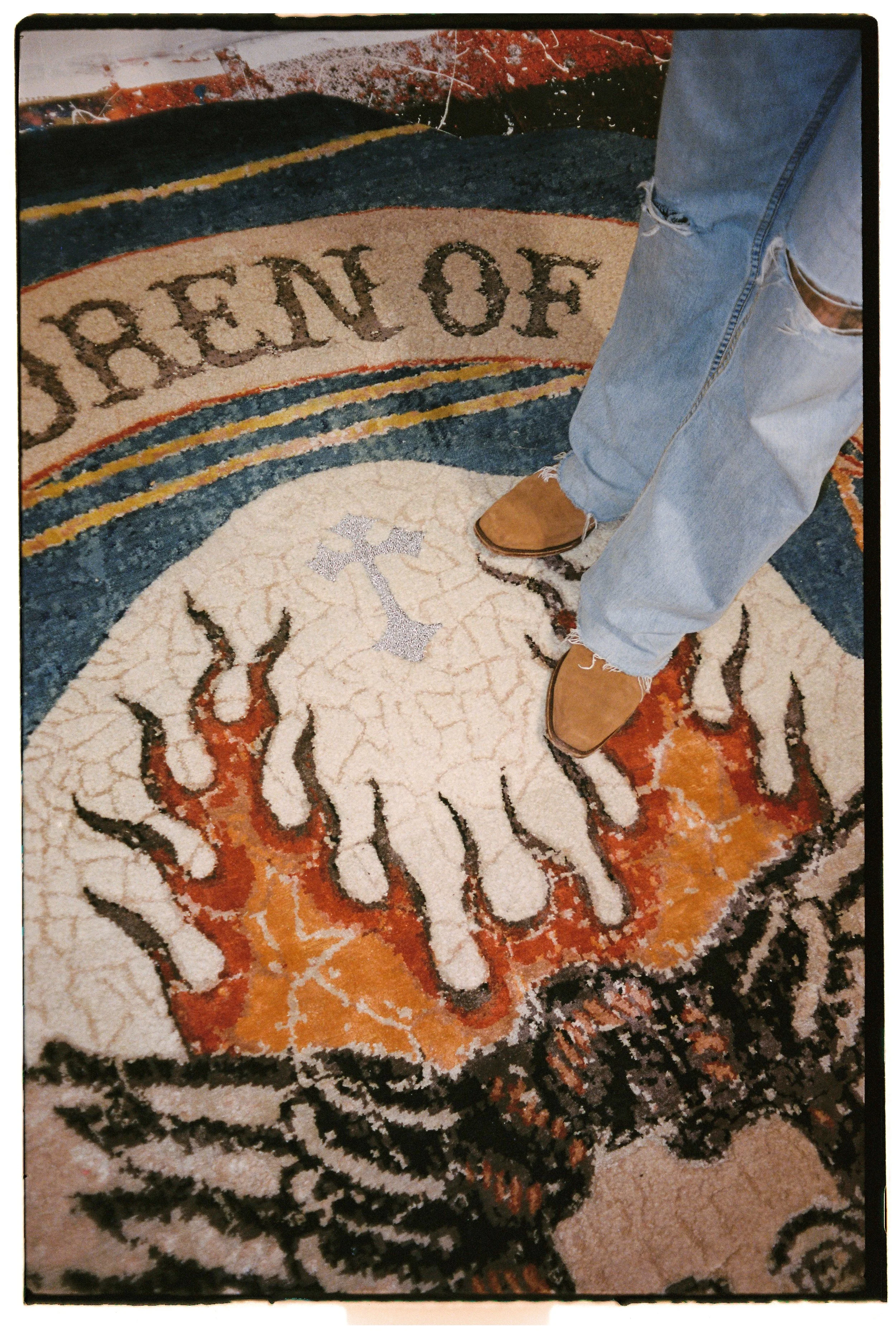 Detail of Children of Sky by Julien Jaca: silver lurex cross and silk flames on a crackled ivory patch, hand-knotted art rug