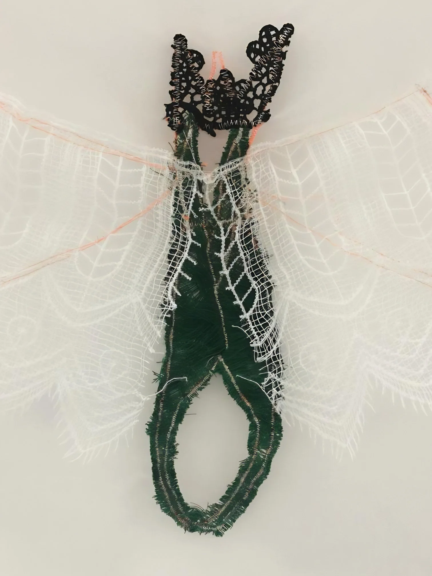 Handcrafted fiber and lace artwork representing an abstract winged figure in a contemporary art gallery