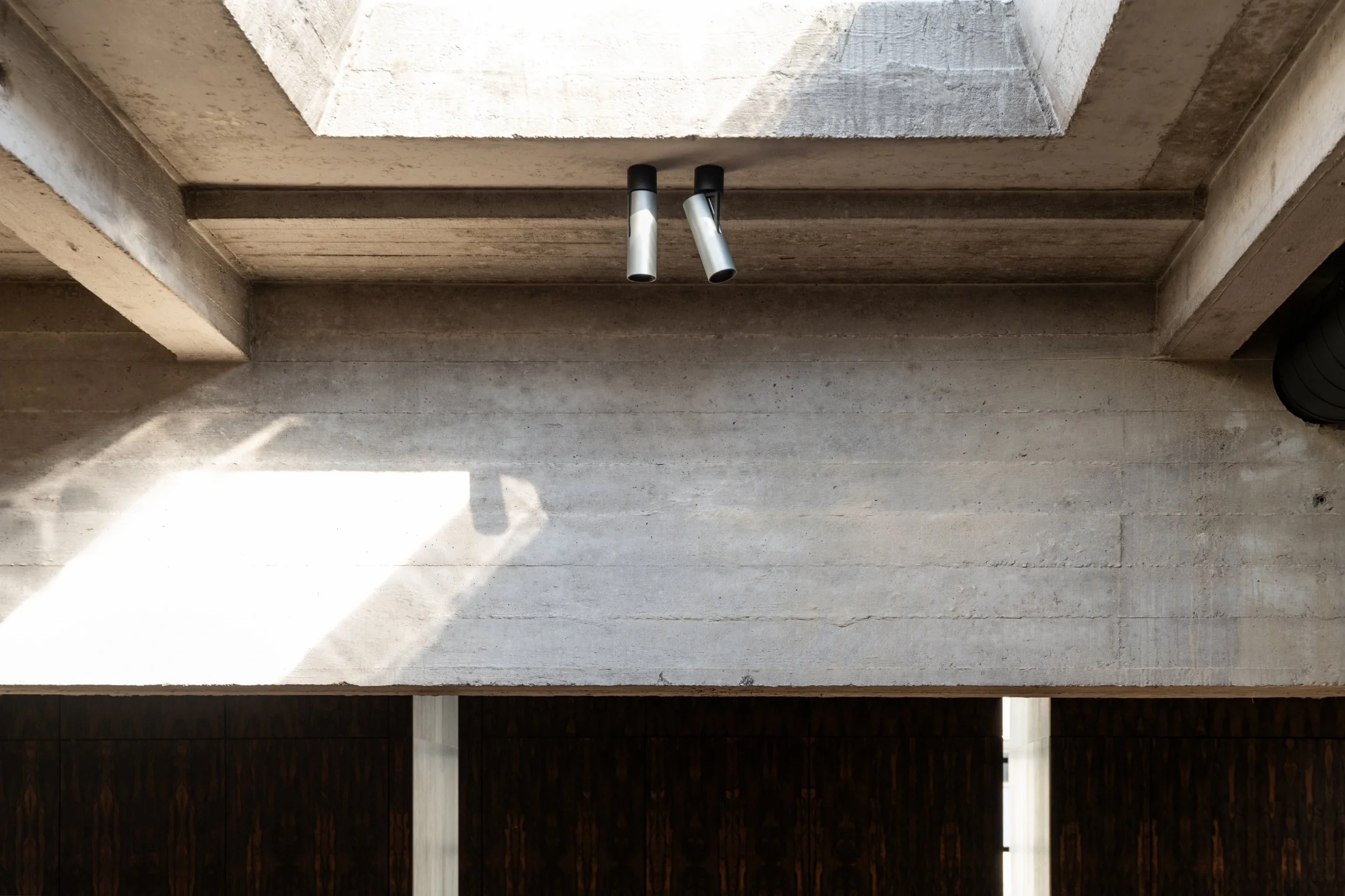 Kreon Holon 60 Directional Surface spotlights in aluminium beneath a skylight between raw concrete beams