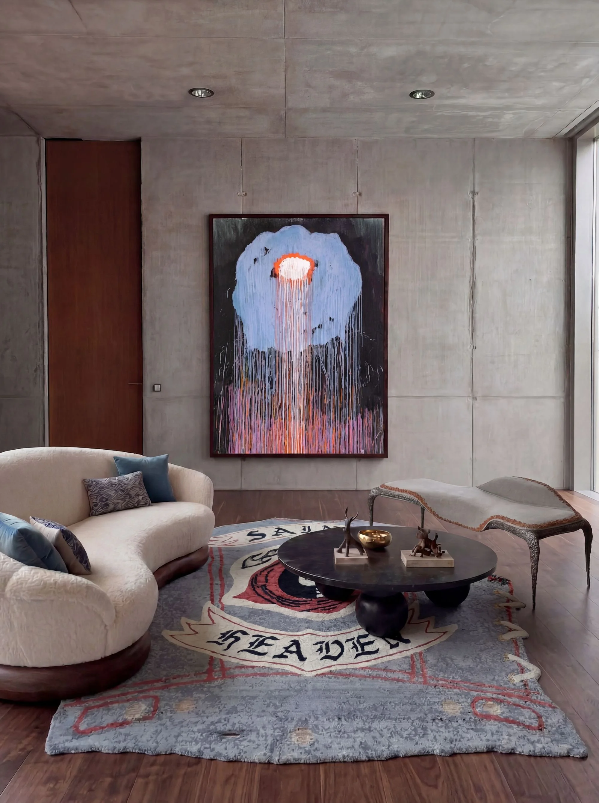 Hand-knotted artist rug by Dinodo Studio with gothic lettering, styled in a concrete living room with a curved sofa, black coffee table and abstract painting.
