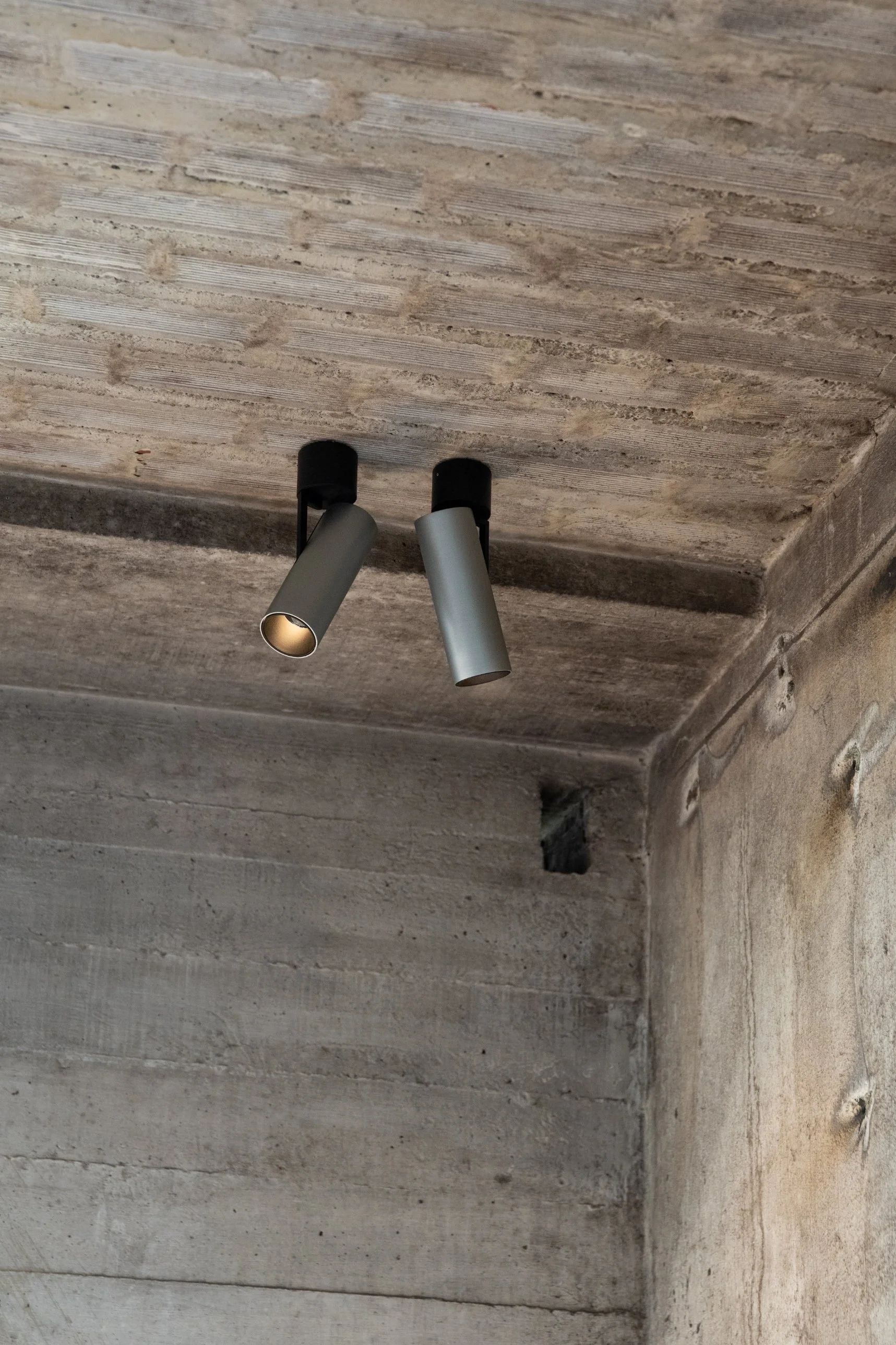Two Kreon Holon 60 Directional Surface spotlights in aluminium on a board-formed concrete ceiling