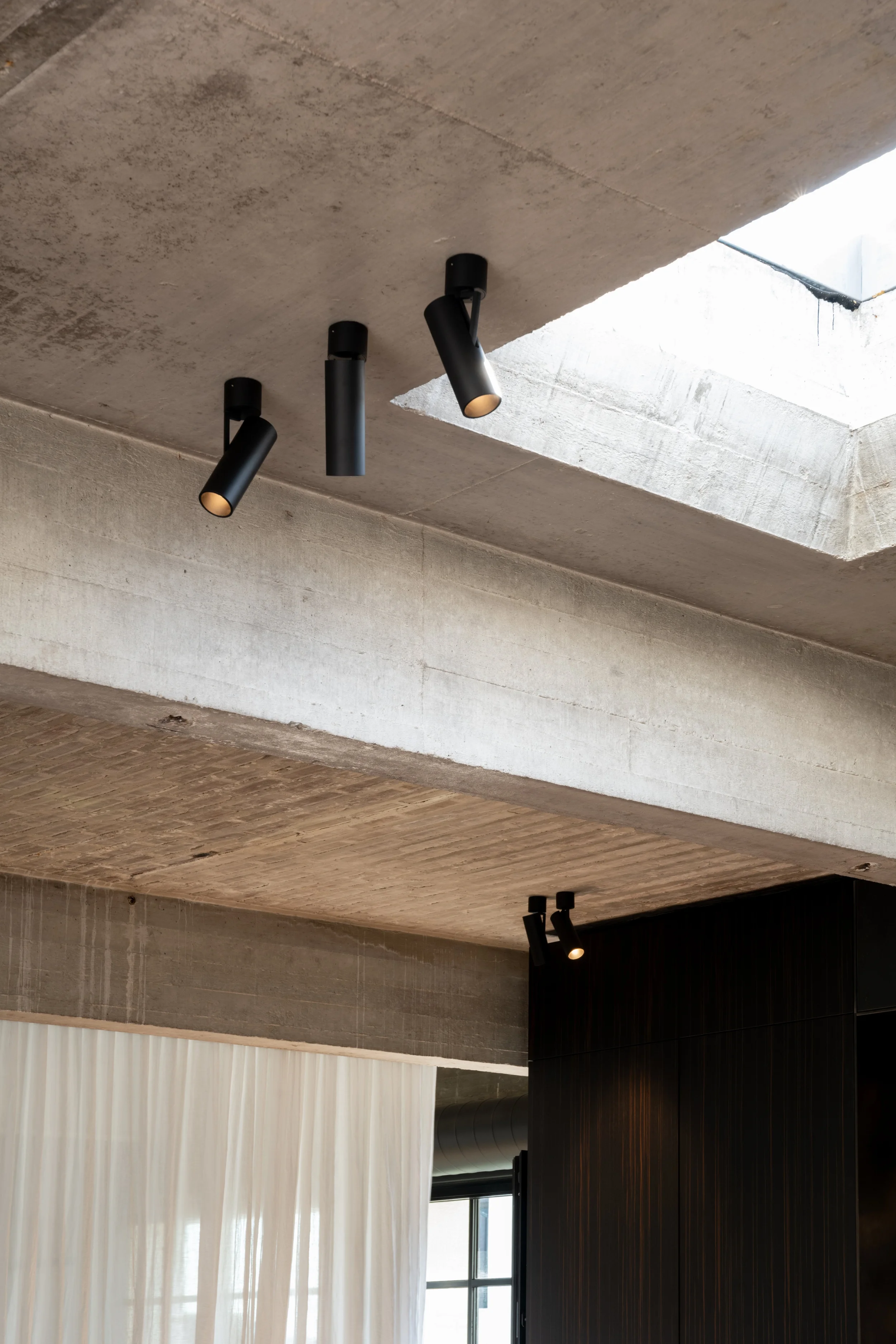Black Kreon Holon 60 Directional Surface spotlights on a concrete ceiling beside a skylight