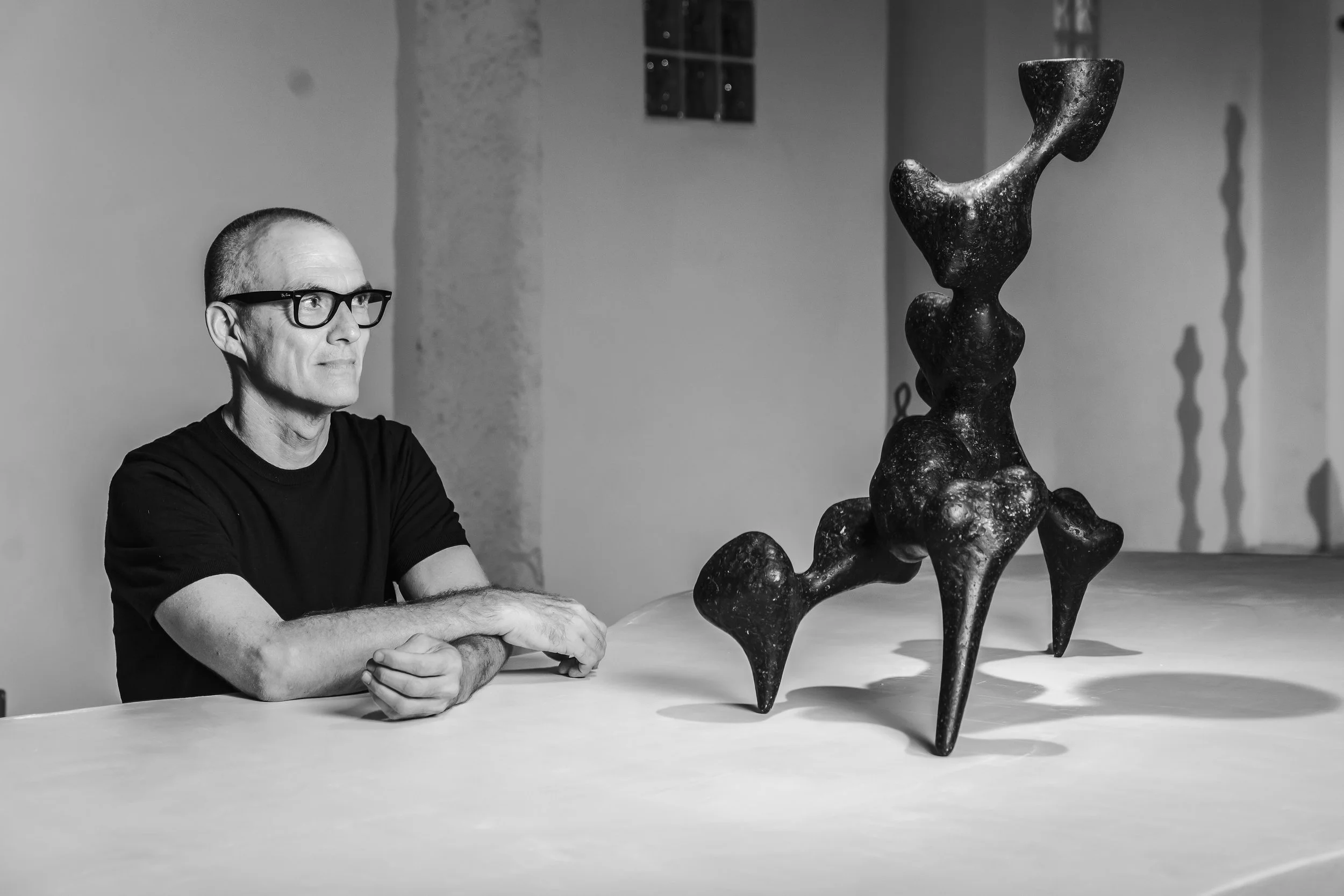Justino del Casar seated at a white table beside a dark organic paper sculpture at BLANCONEGRO, Barcelona.