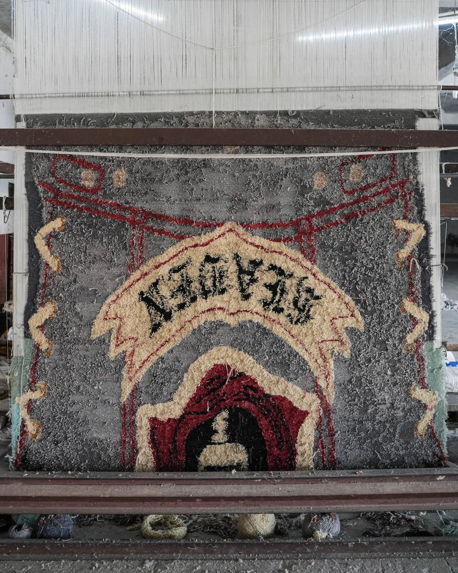 Dinodo Studio rug being hand-knotted on a vertical loom in the atelier, with cotton warp threads above and balls of wool yarn at its base.