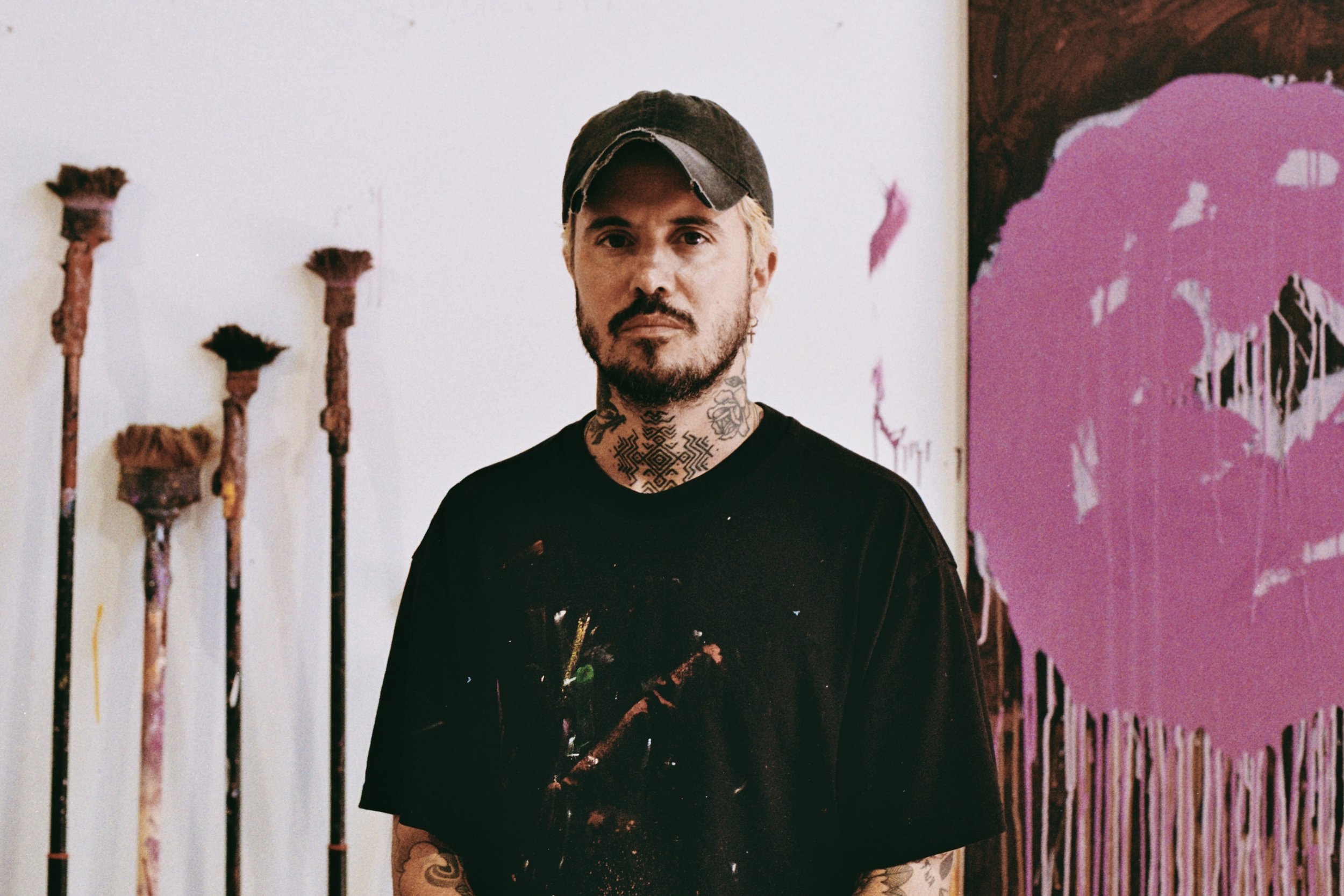 French painter Julien Jaca, seen from behind in a cap, in front of his dripping flower paintings, the artist behind the Crying Flowers art rugs for Dinodo Studio
