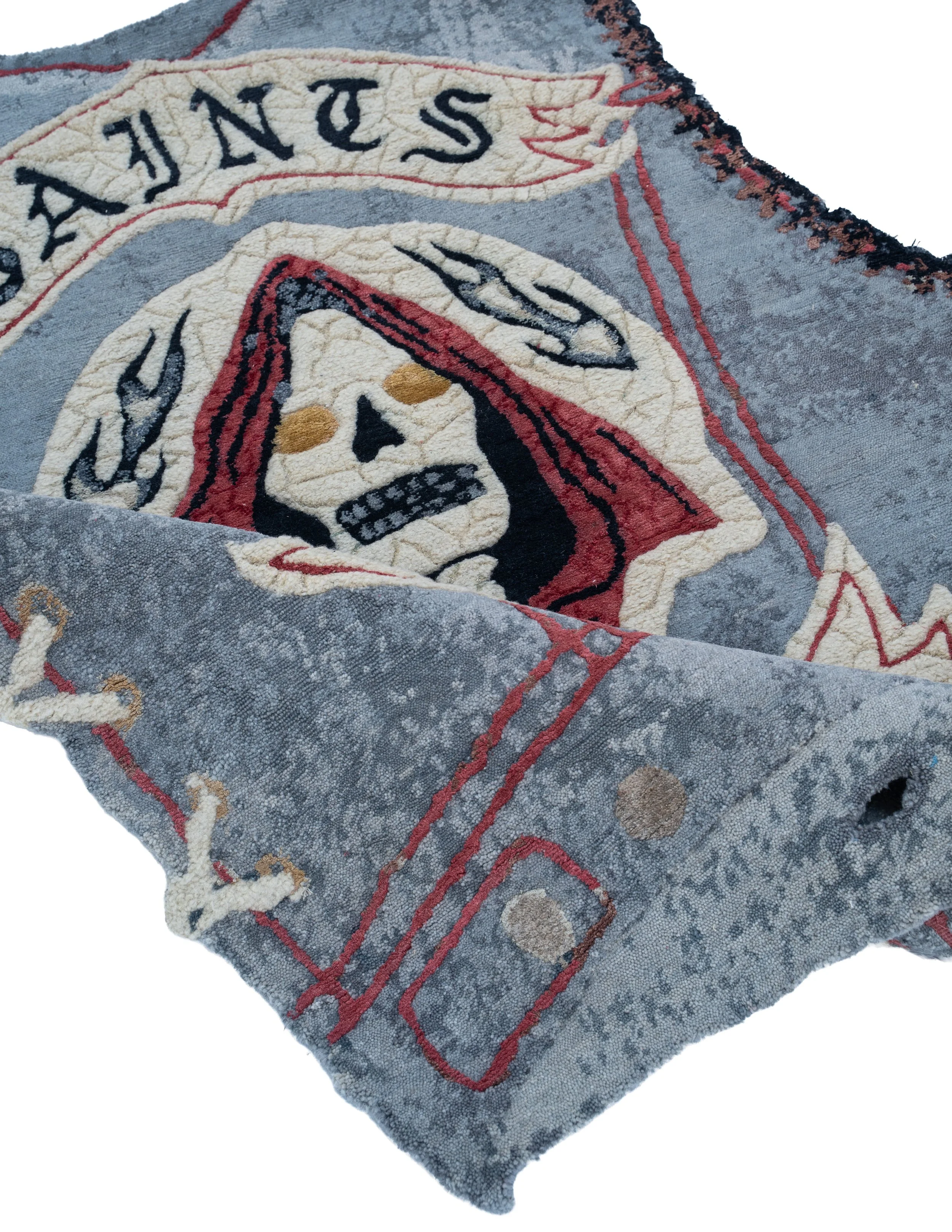 Close-up of Saints by Julien Jaca folded over: hand-knotted pile in wool, silk, alpaca and nettle with skull, flames and red stitching