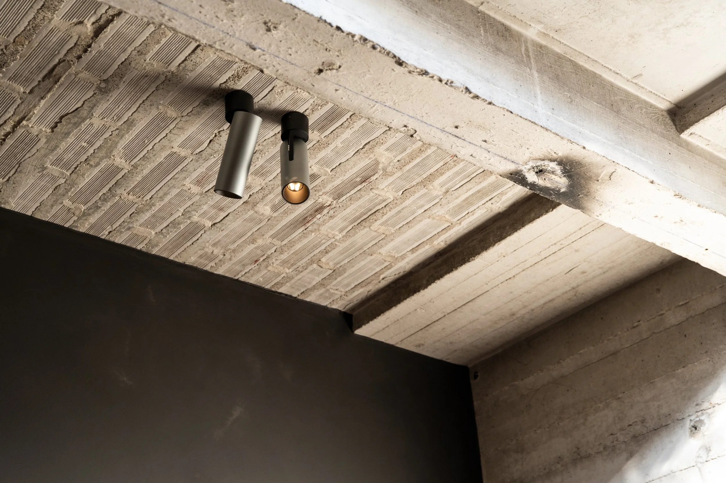 Kreon Holon 60 Directional Surface spotlights in aluminium, one lit, on a textured concrete ceiling