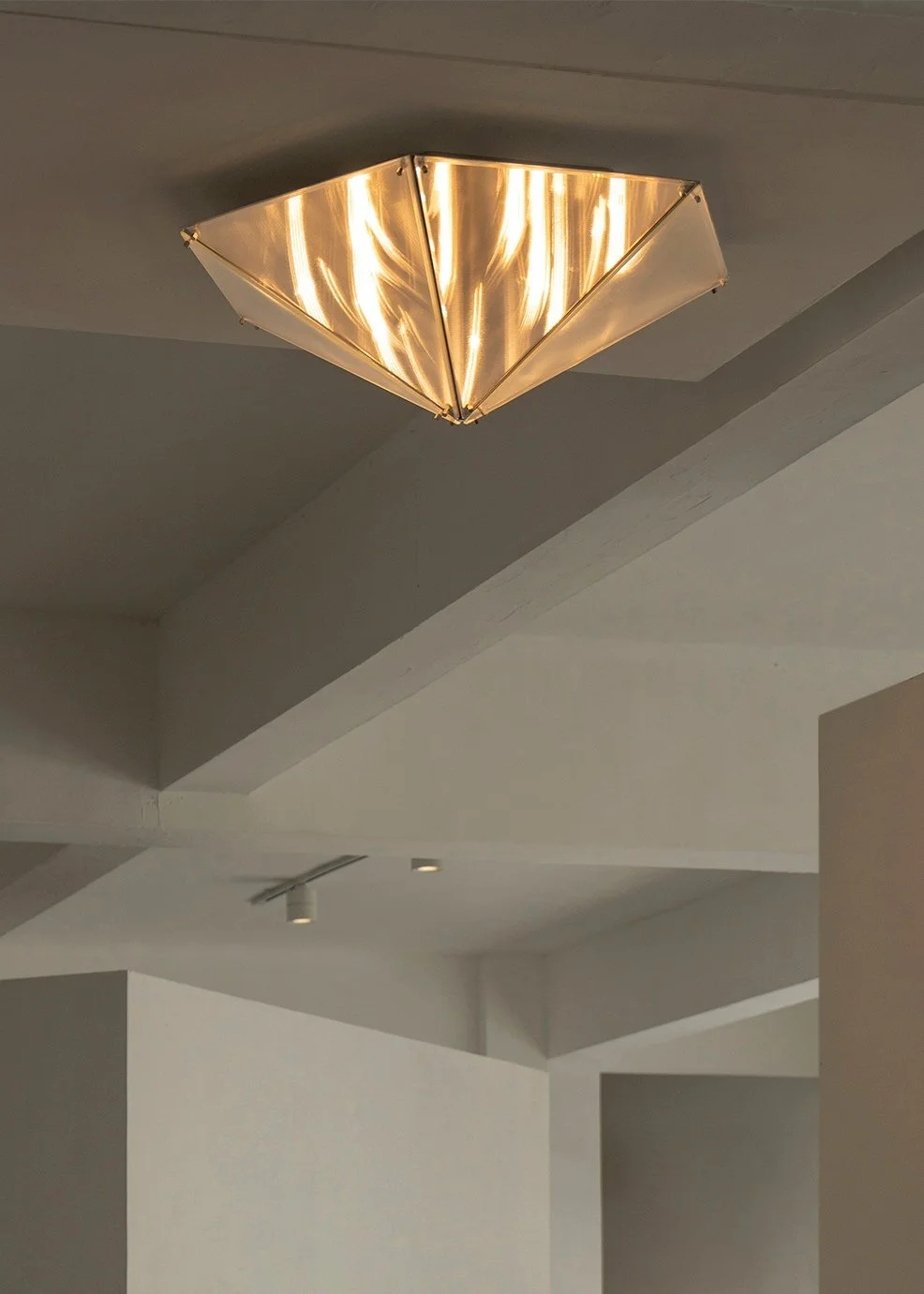 Warm illuminated ceiling sculpture by Sing Chan installed in a minimal interior.