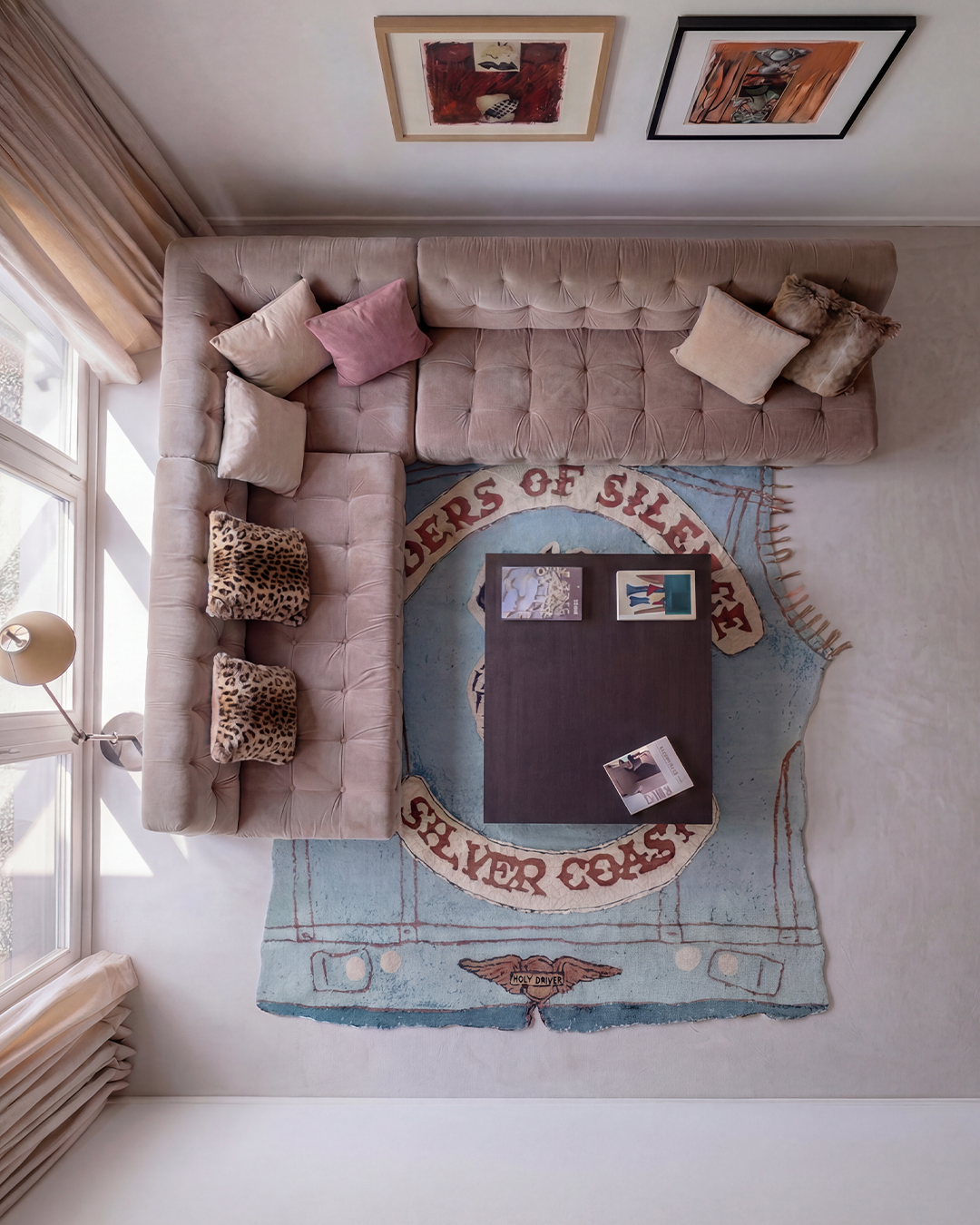 Aerial view of Riders of Silence, a denim vest-shaped artist rug by Julien Jaca, under a dark coffee table beside a tufted corner sofa