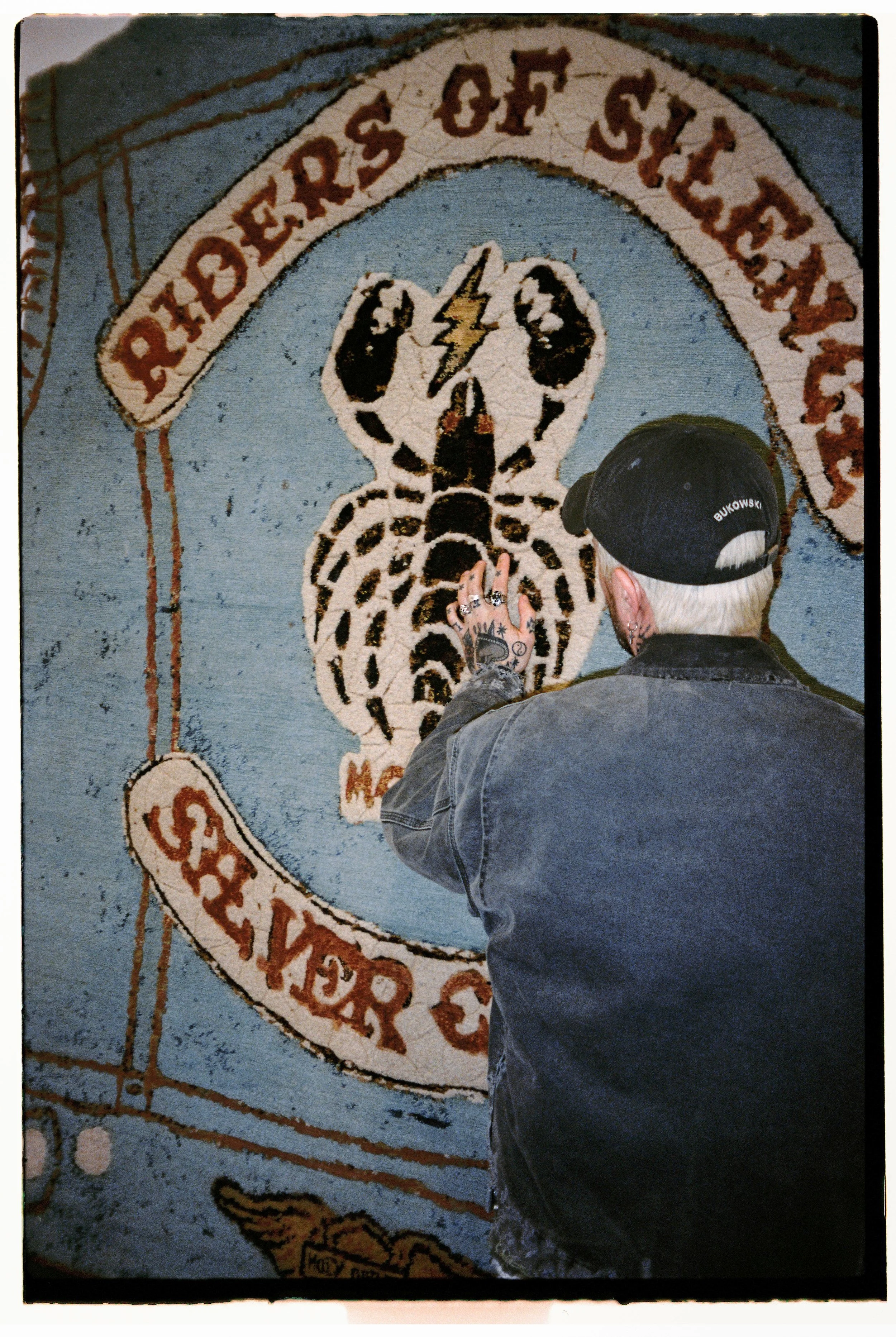 Artist Julien Jaca facing his Riders of Silence hand-knotted rug for Dinodo Studio, hung on the wall as a large tapestry