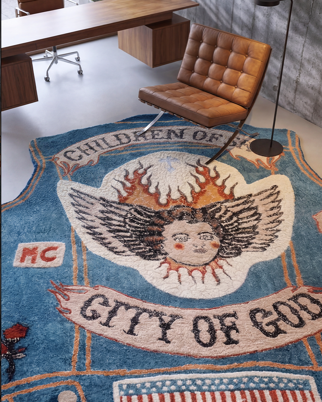 Children of Sky, a denim vest-shaped artist rug by Julien Jaca, in a concrete office with a tan leather lounge chair and walnut desk