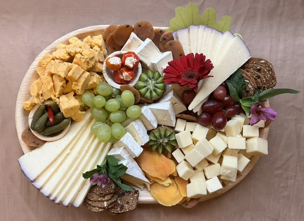 A cheese and fruit platter with various cheeses, grapes, crackers, and garnishes