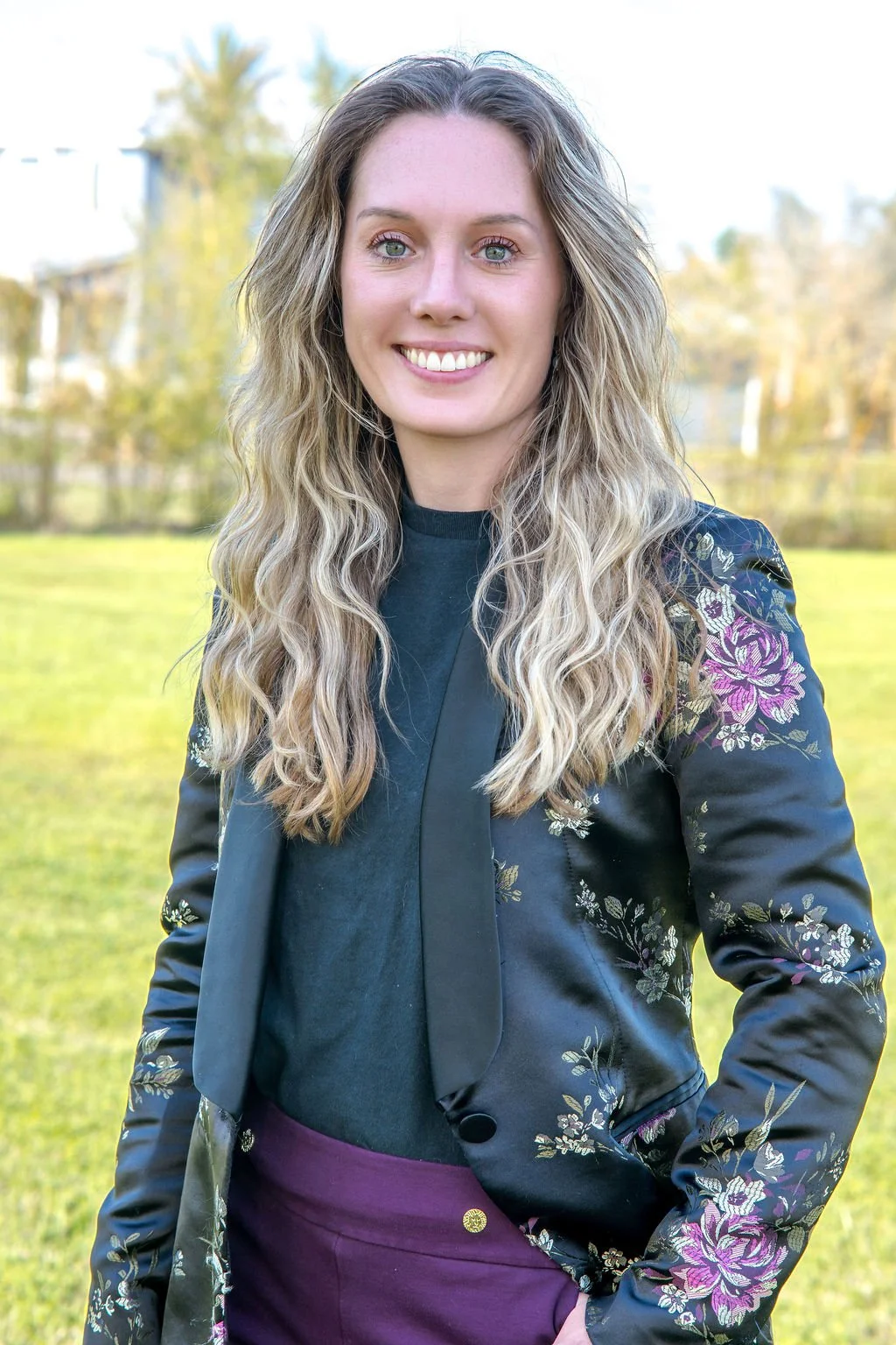 A woman with long, wavy blonde hair smiling and taking a selfie against a white paneled door background.