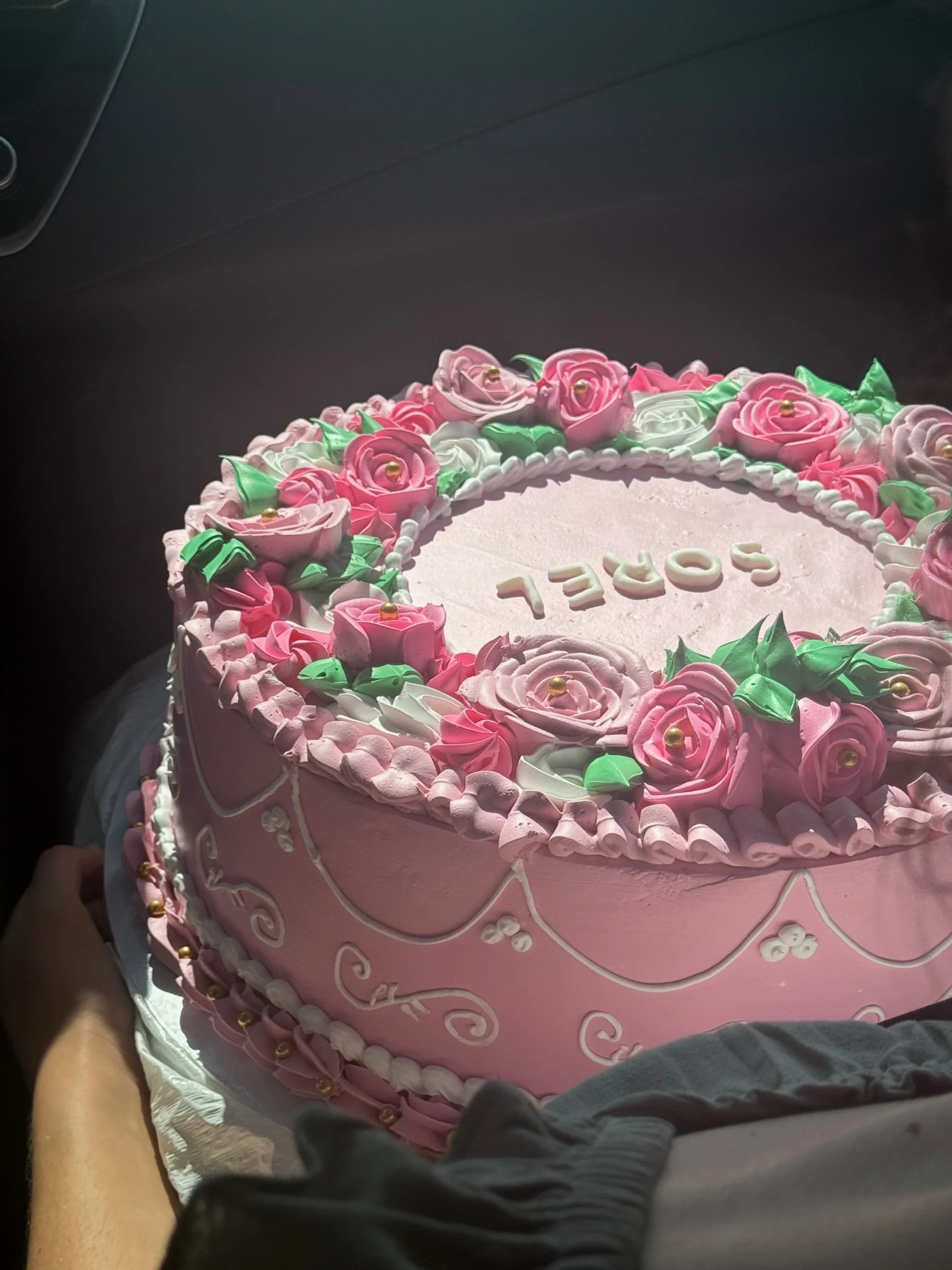 pink cake decorated with pink and white flowers made out of frosting, decorative frosting patterns along the side, cake reads "Sorel"