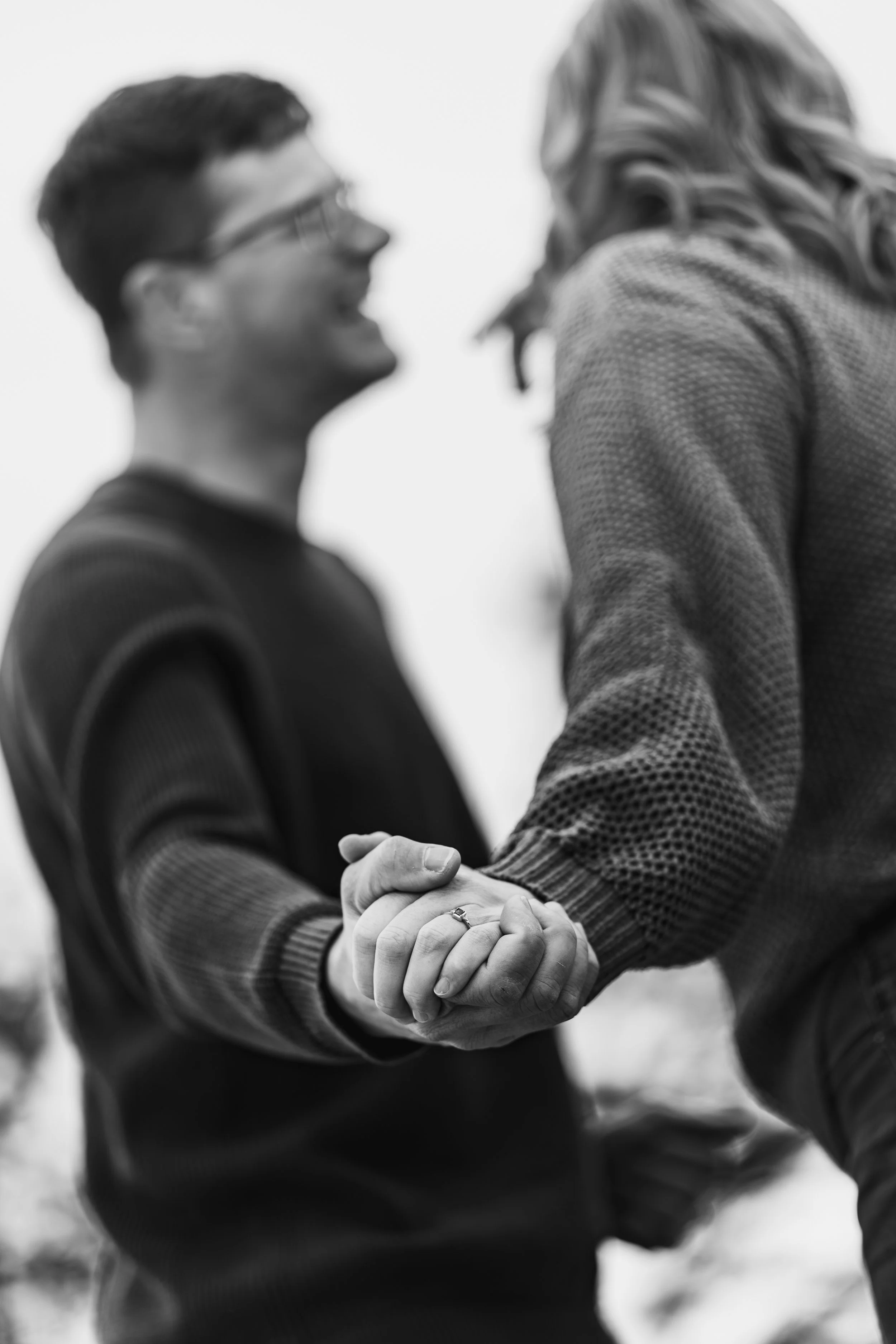 Black and white photo of a couple holding hands, smiling, and looking at each other outdoors