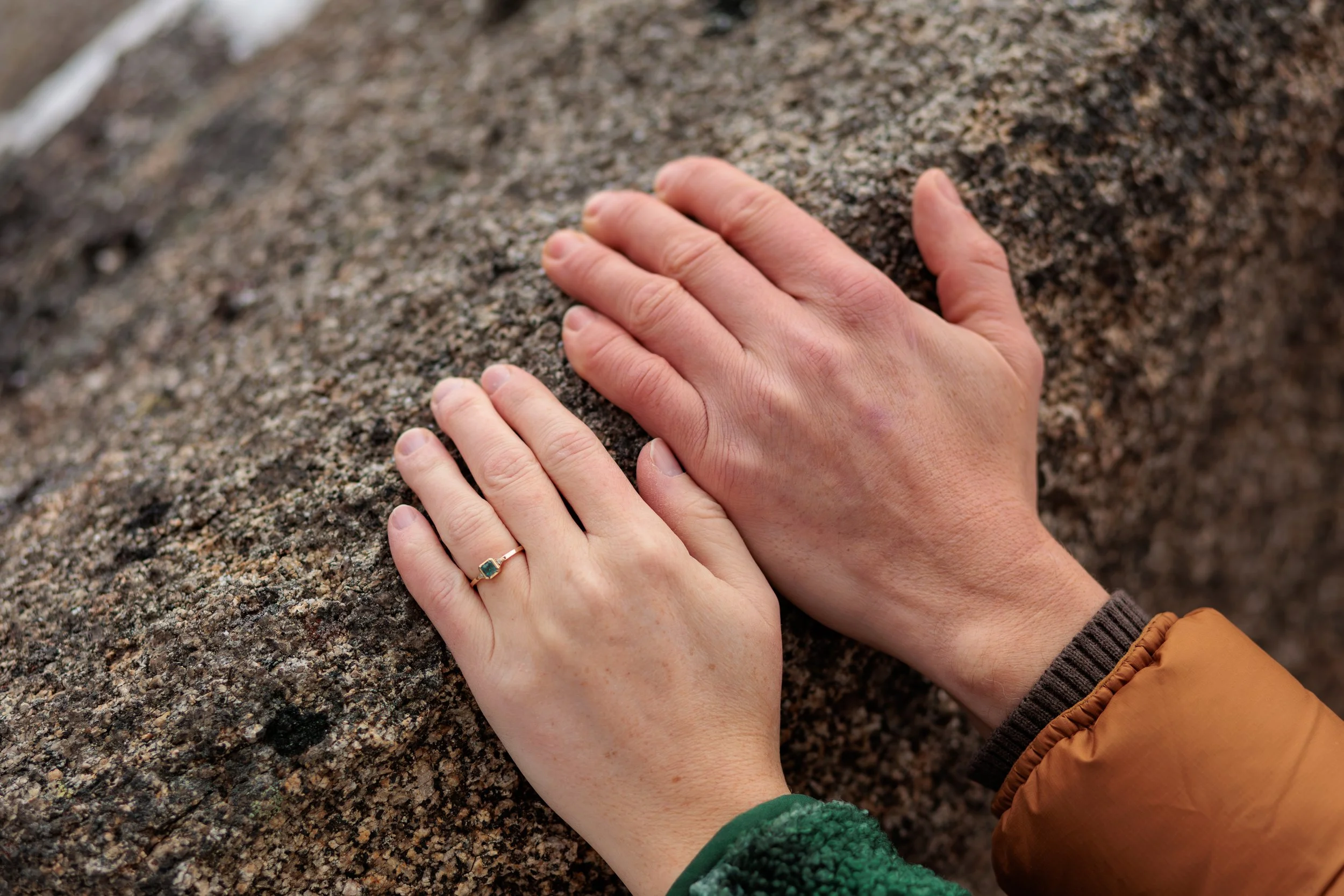 Close-up of two hands, one with a ring, gripping a rough, textured rock surface.