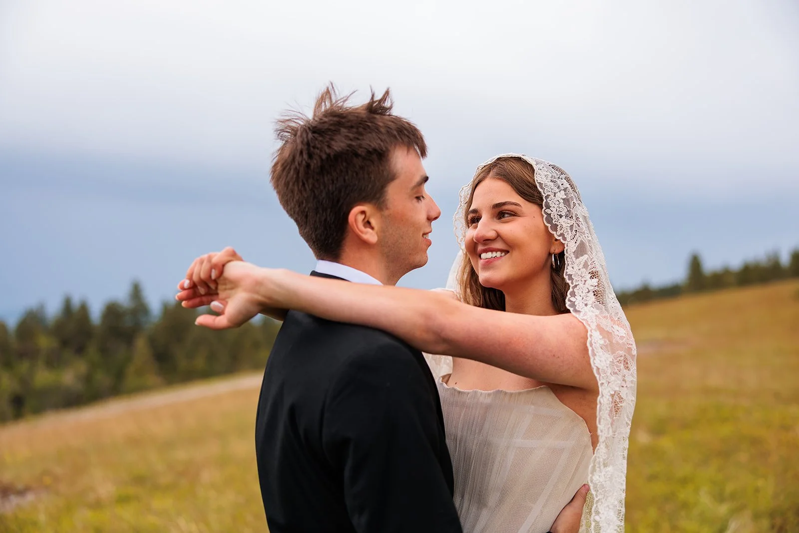 A bride and groom embracing outdoors in a field with a cloudy sky in the background