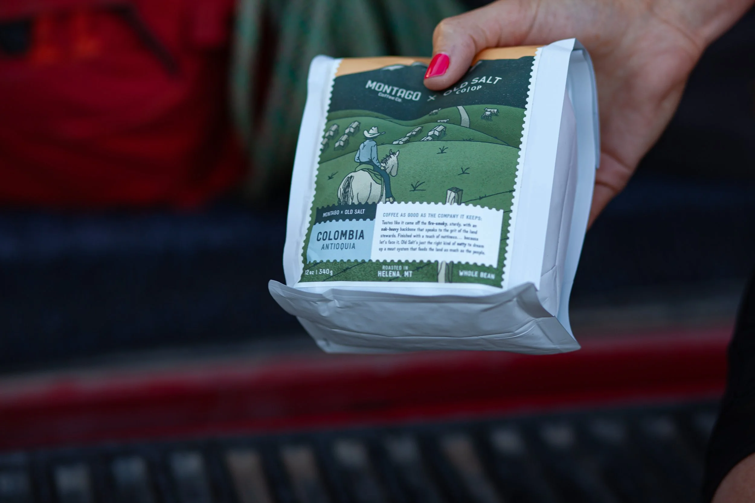 Close-up of a person holding a bag of coffee with a mountain and farm illustration, details about the coffee, and a person riding a horse on the label.