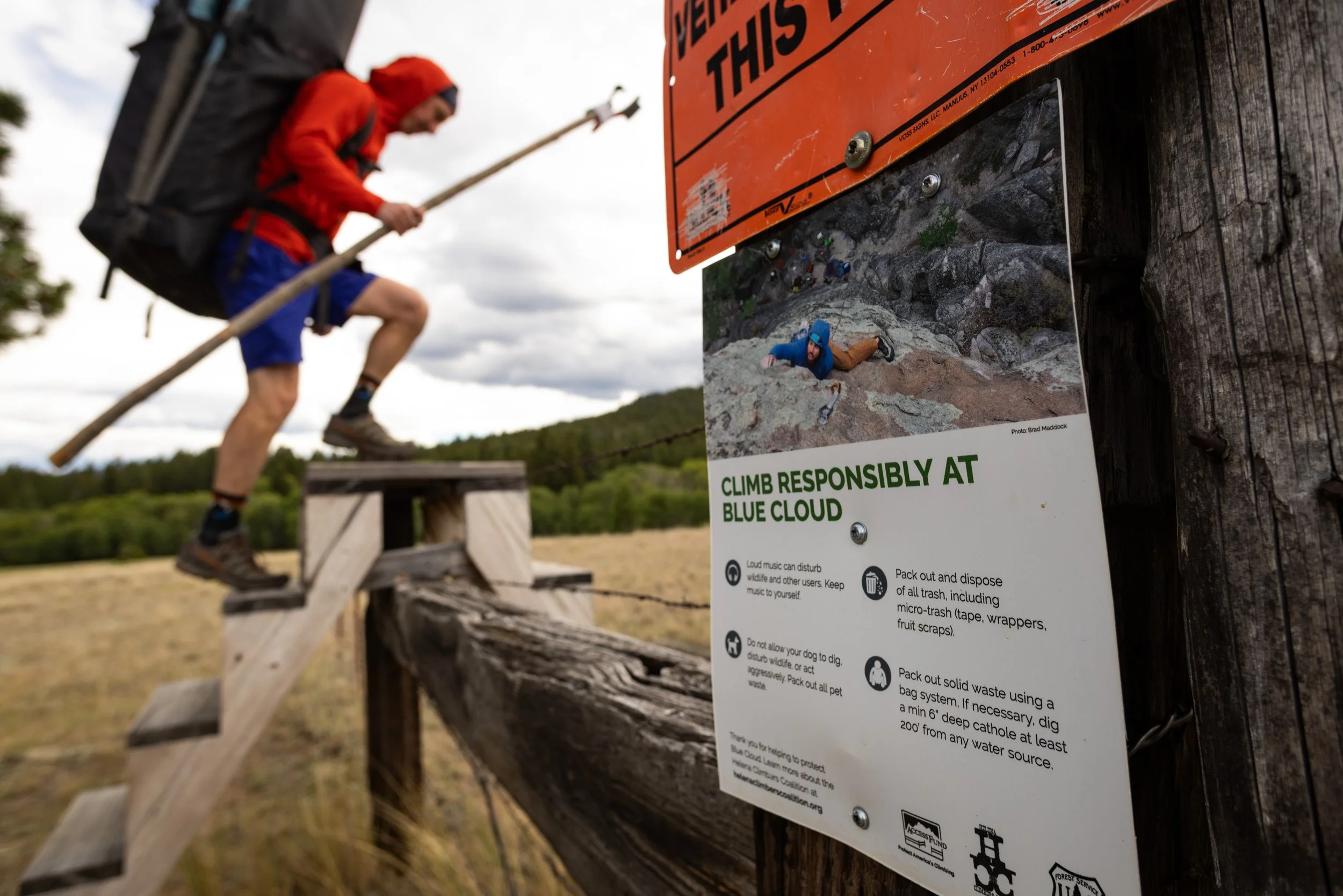 A person climbing over a wooden obstacle with a badge on a fence that has instructions for responsible climbing at Blue Cloud, including warnings about loud music and trash disposal.