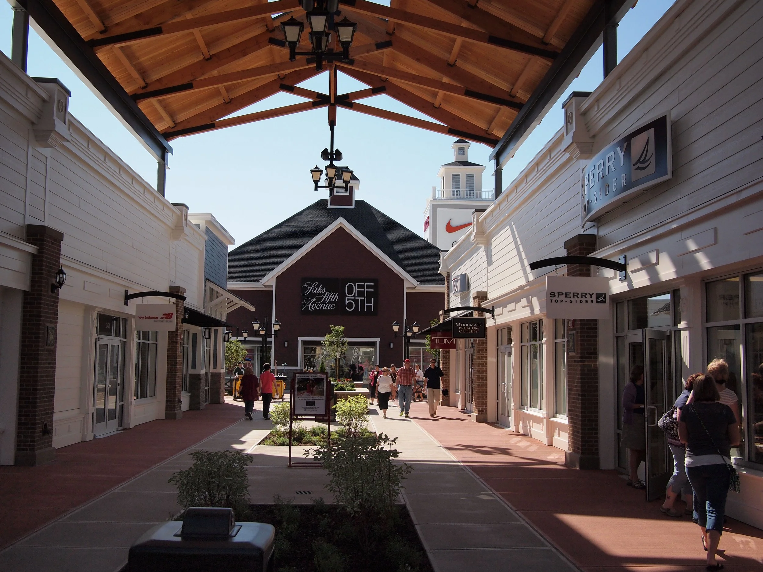 Outdoor walkway at the Merrimack Premium Outlets in New Hampshire, featuring storefronts like Saks Fifth Avenue OFF 5TH and Sperry 