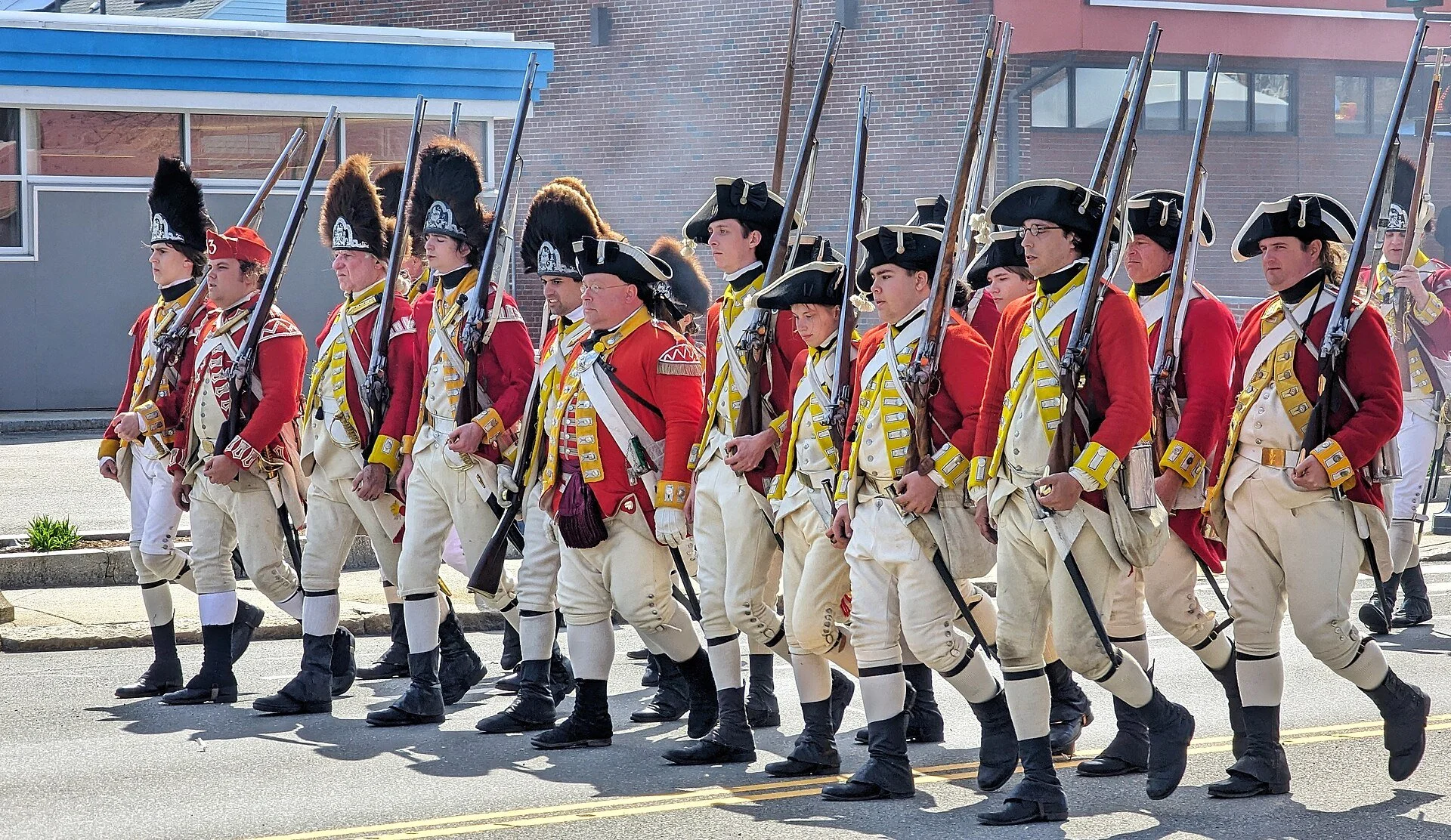 A group of living history reenactors dressed as British Redcoat soldiers from the American Revolutionary War marching in a parade