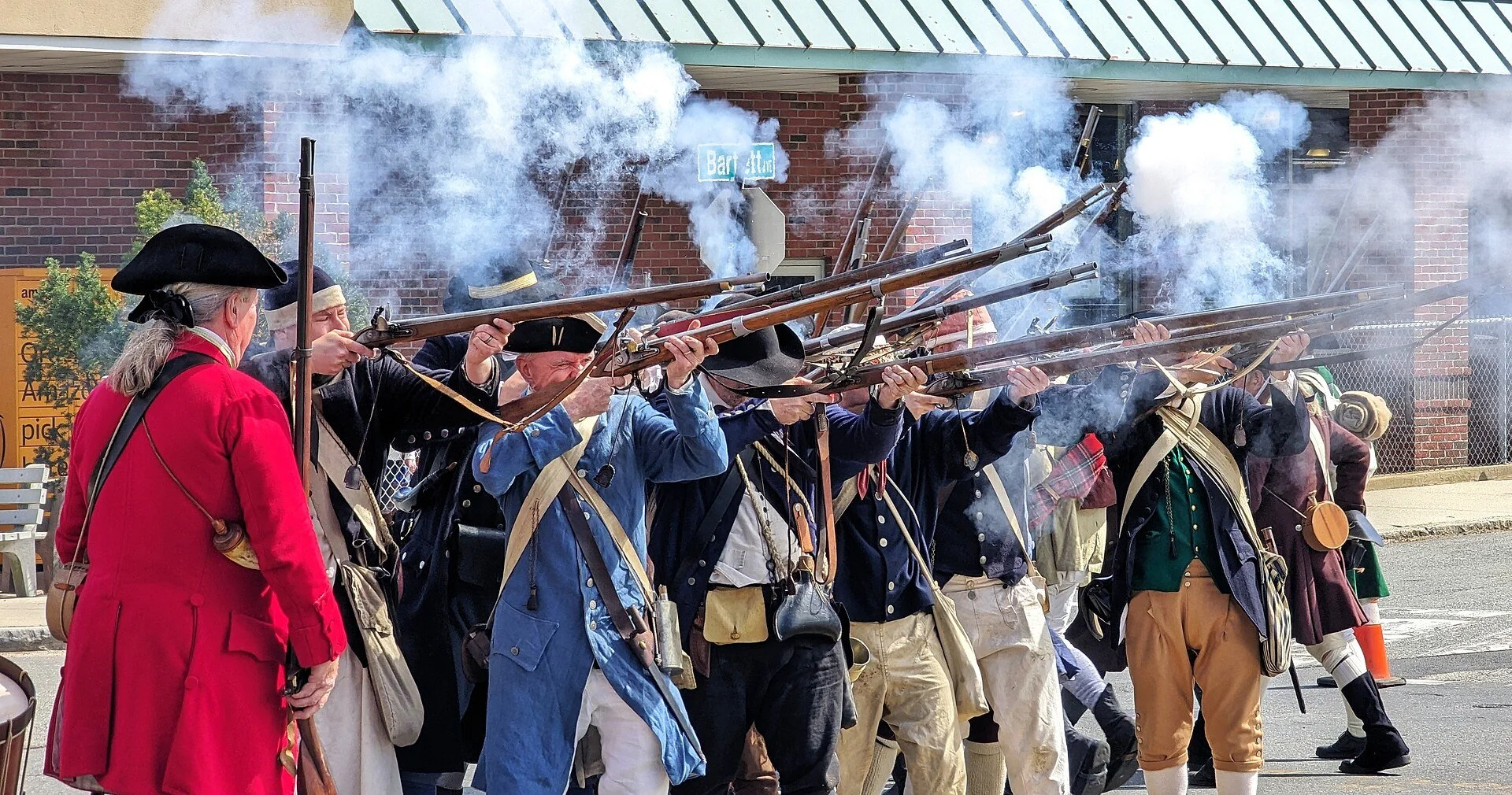 Historical reenactors firing muskets during a Patriots' Day commemoration event in Arlington, Massachusetts