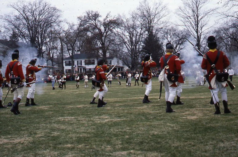 Historical reenactment of the Battle of Lexington, featuring participants dressed as British Redcoats firing muskets on the Lexington Battle Green in Massachusetts
