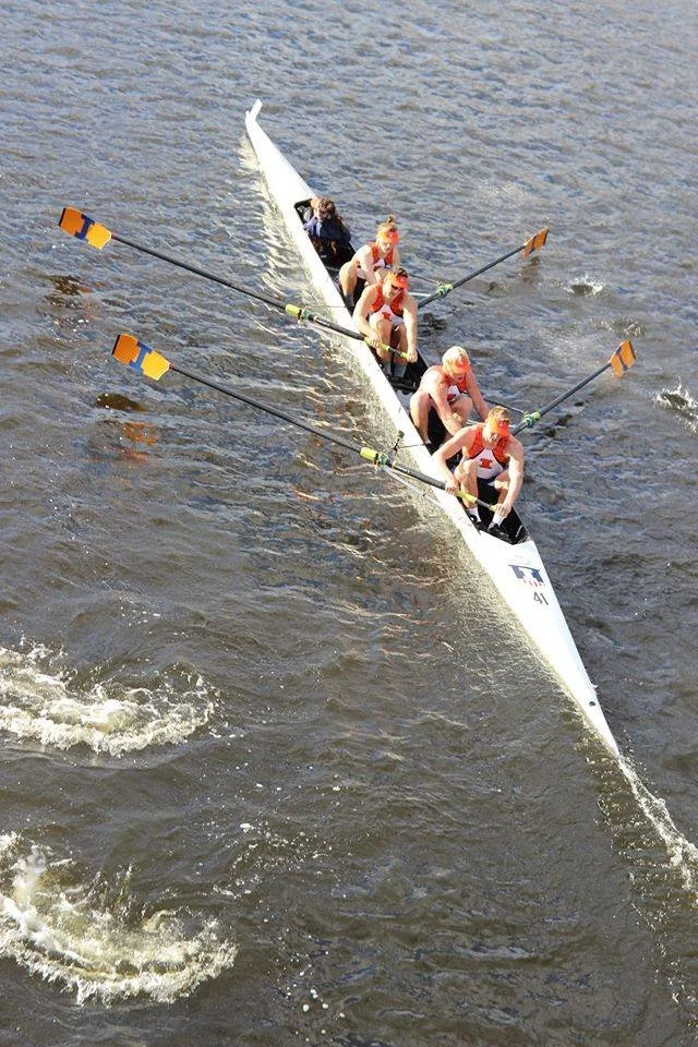 Four-person rowing team (coxed four or a sweep four boat) navigating on the water with oars extended.