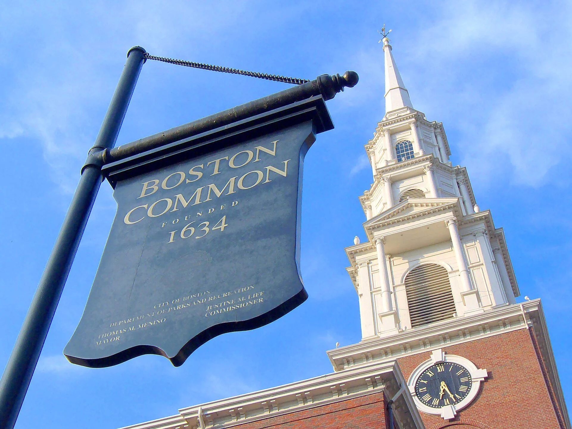 Black historical marker sign for Boston Common with the steeple of the historic Park Street Church in the background