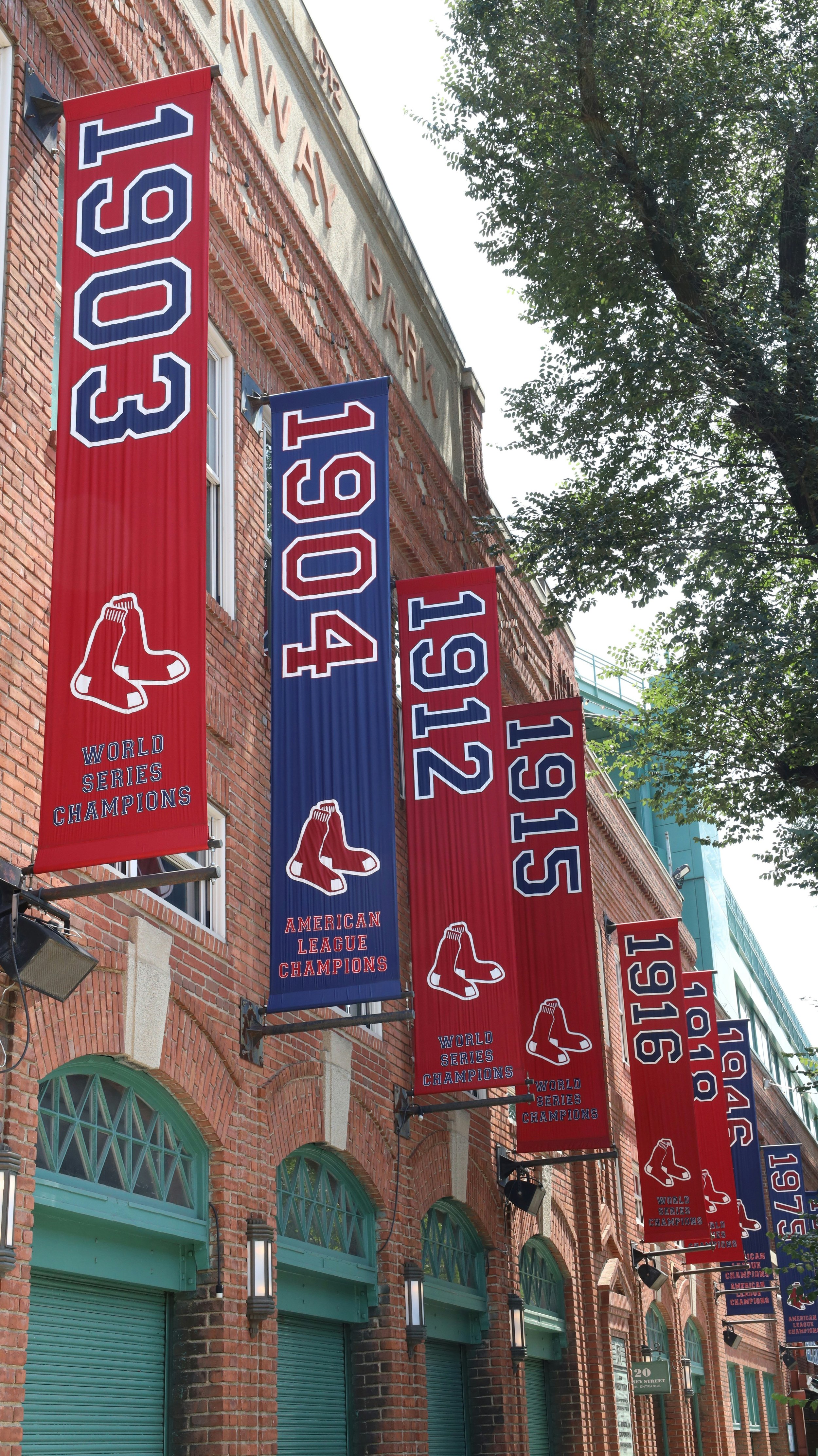 World Series championship banners hanging outside Fenway Park in Boston, featuring years like 1903, 1904, 1912, and 1915 alongside the Boston Red Sox logo.