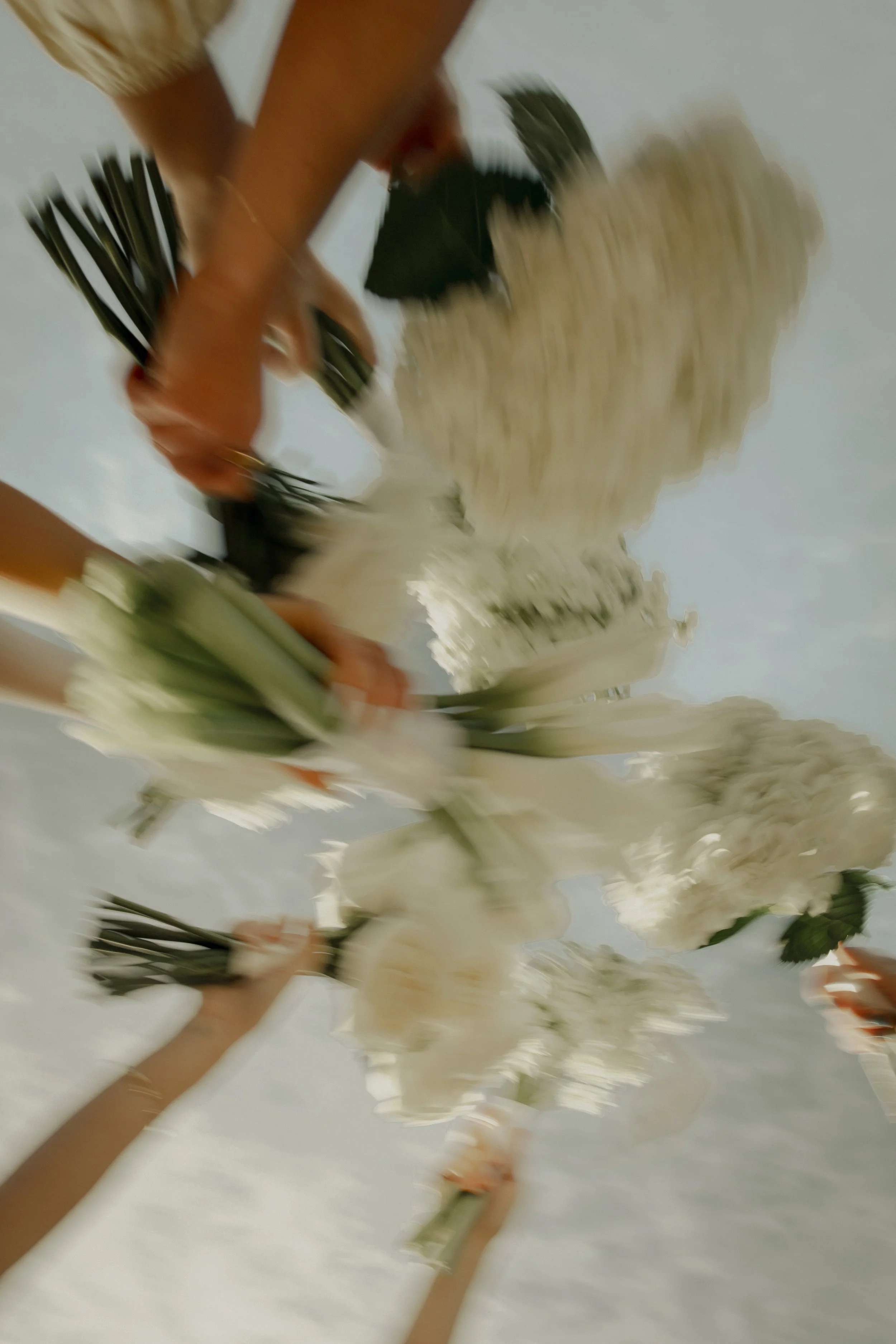 People holding white flower bouquets against a cloudy sky.