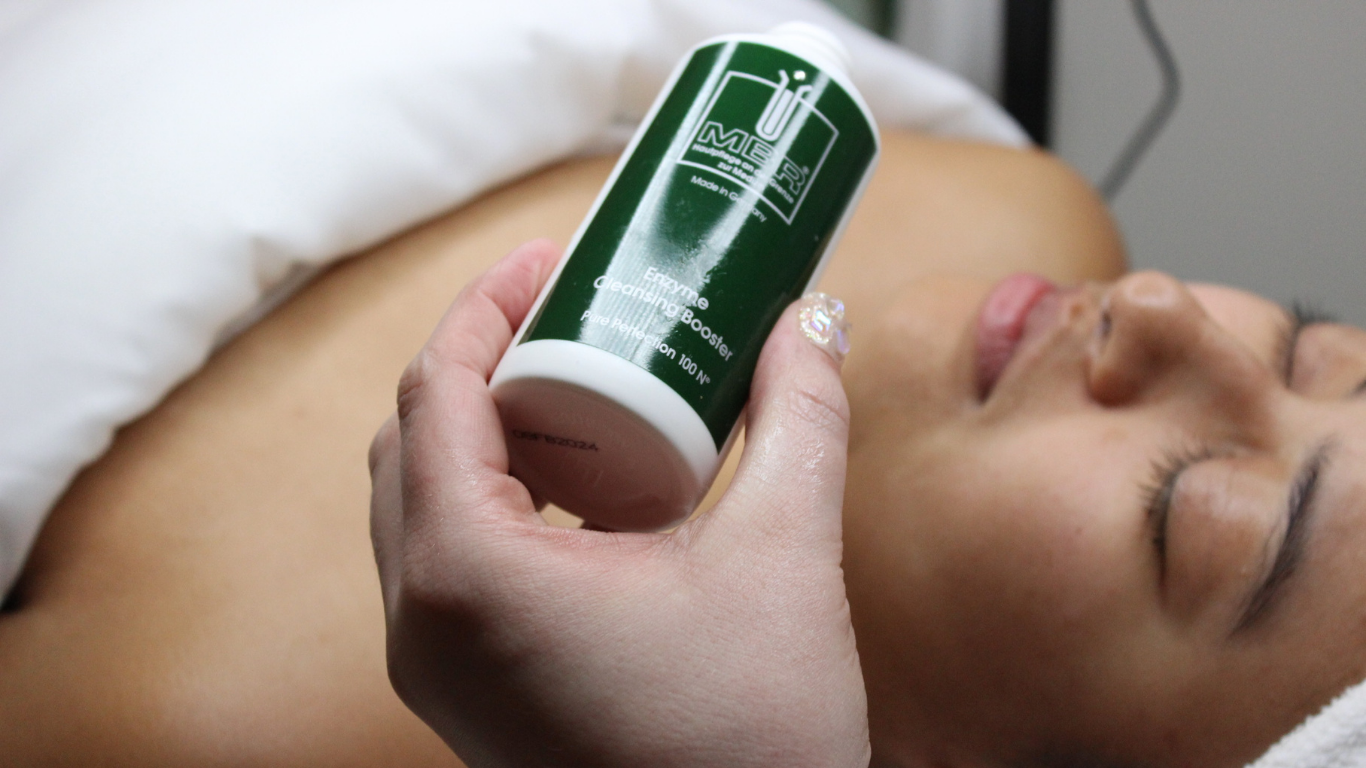 Esthetician Aislinn showcases MBR’s Enzyme Cleansing Booster before applying it to a woman during a facial treatment
