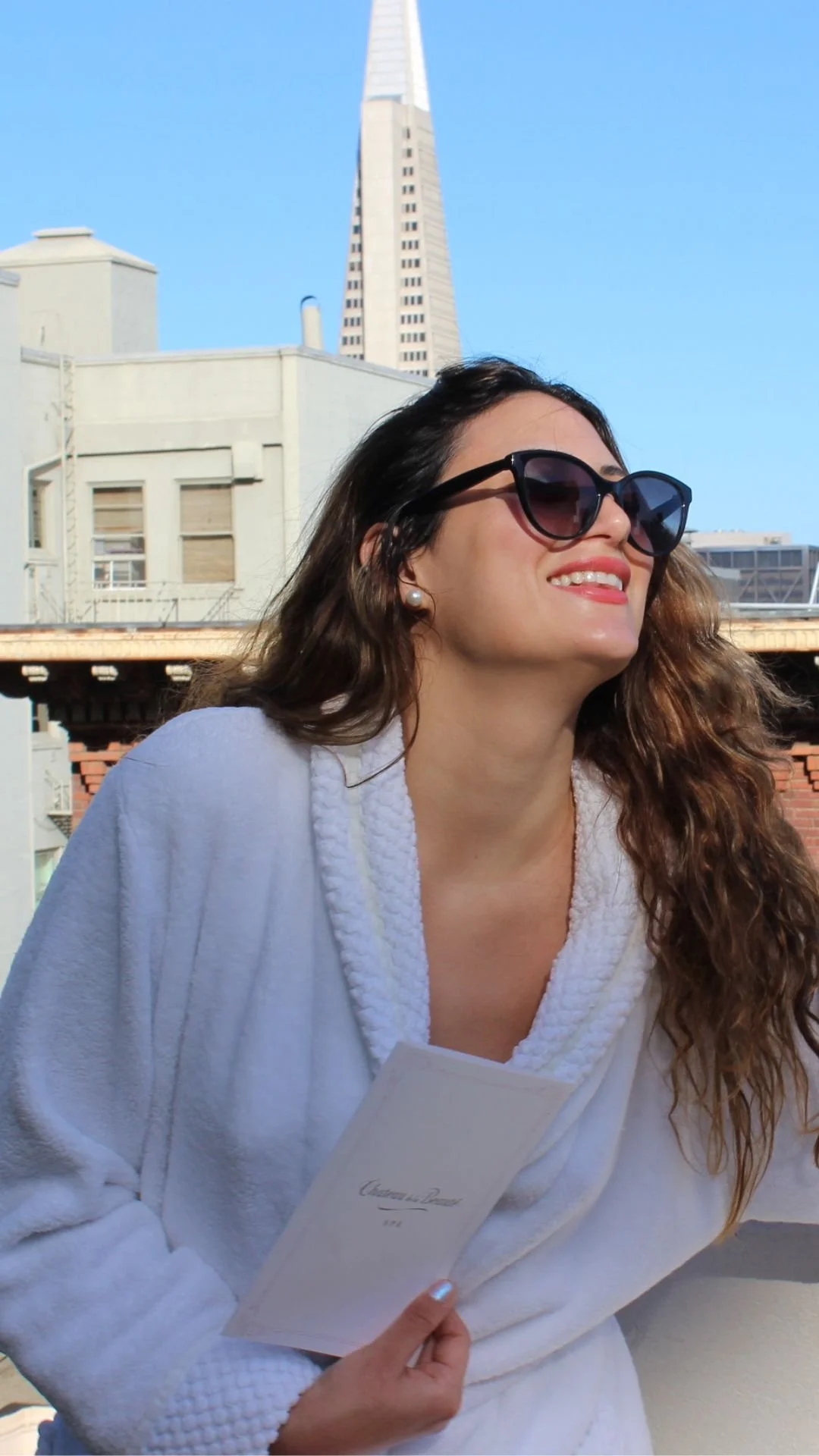 A guest relaxes in the Rooftop Garden at the Fairmont San Francisco, enjoying sunshine and stunning city skyline views after a refreshing facial treatment