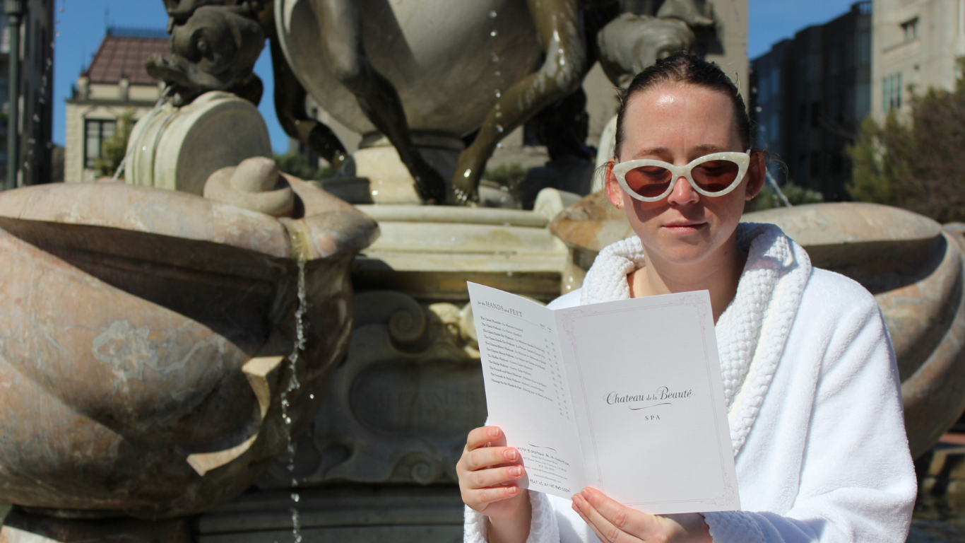A woman sits in Huntington Park, Nob Hill, reading the Chateau de la Beauté spa menu, anticipating a day of luxurious pampering and skin renewal