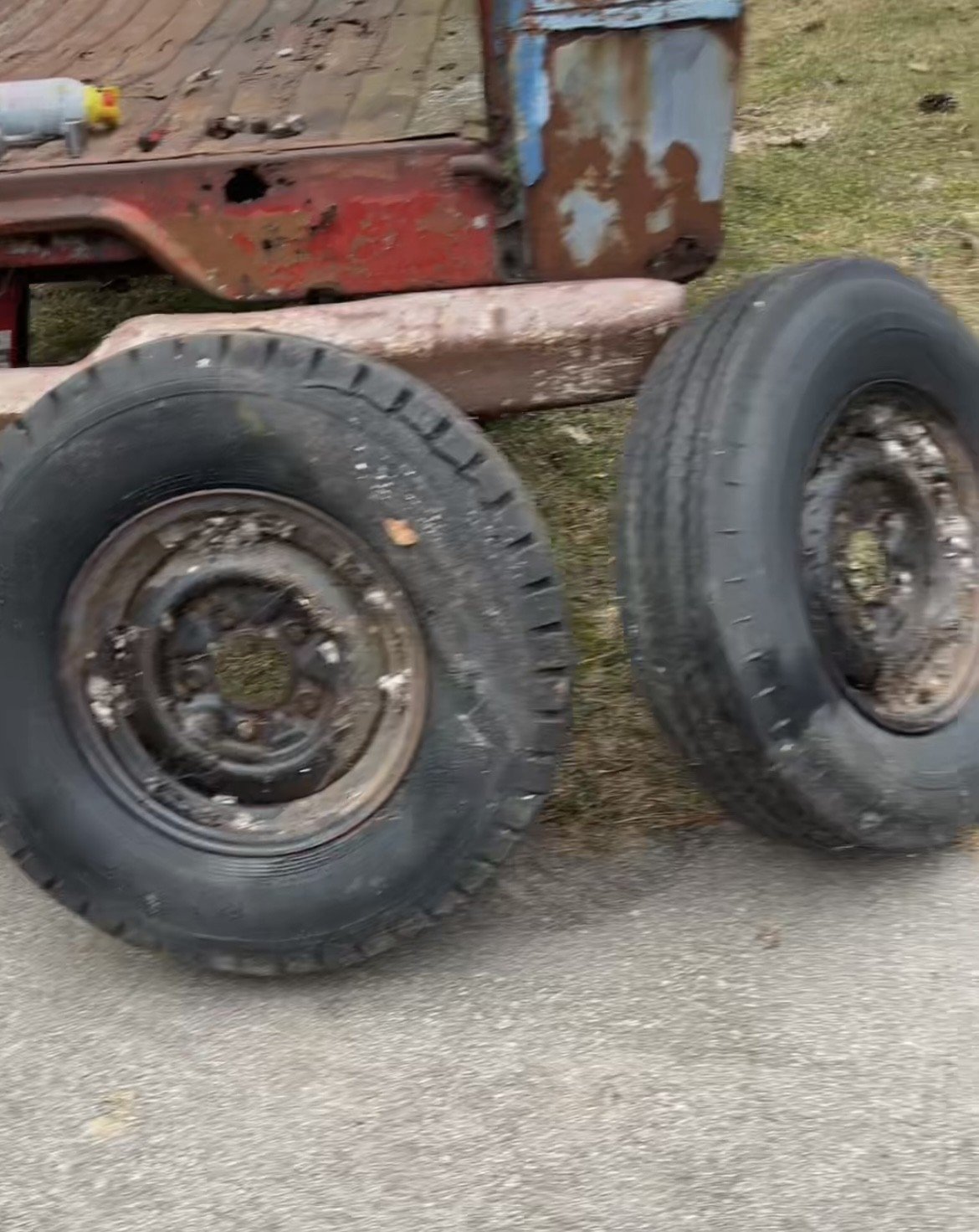 Two old vehicle tires on the ground beside a rusty, dilapidated truck bed.