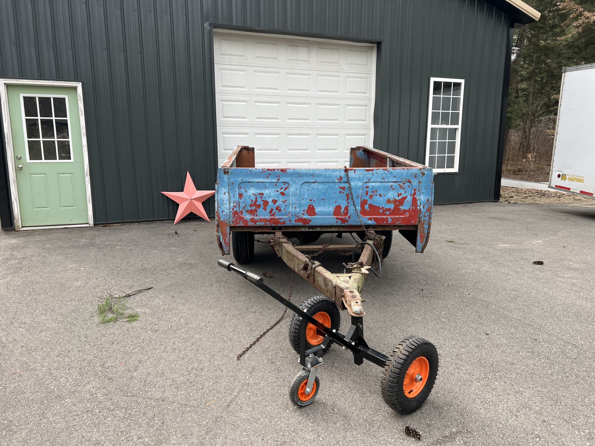 Rusty old blue truck bed on wheels in front of a green building with a pink star decoration next to a green door.