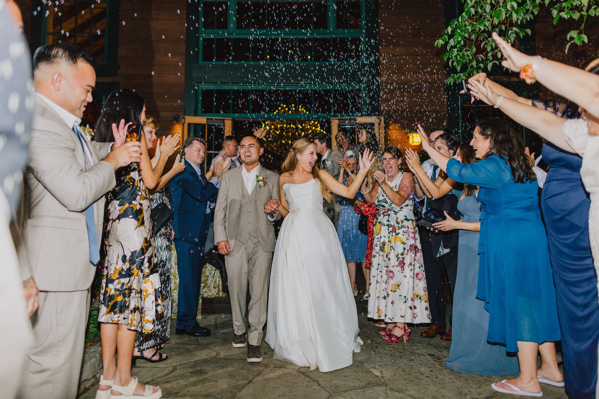 Bride and groom walking through a crowd of smiling guests throwing confetti at night.
