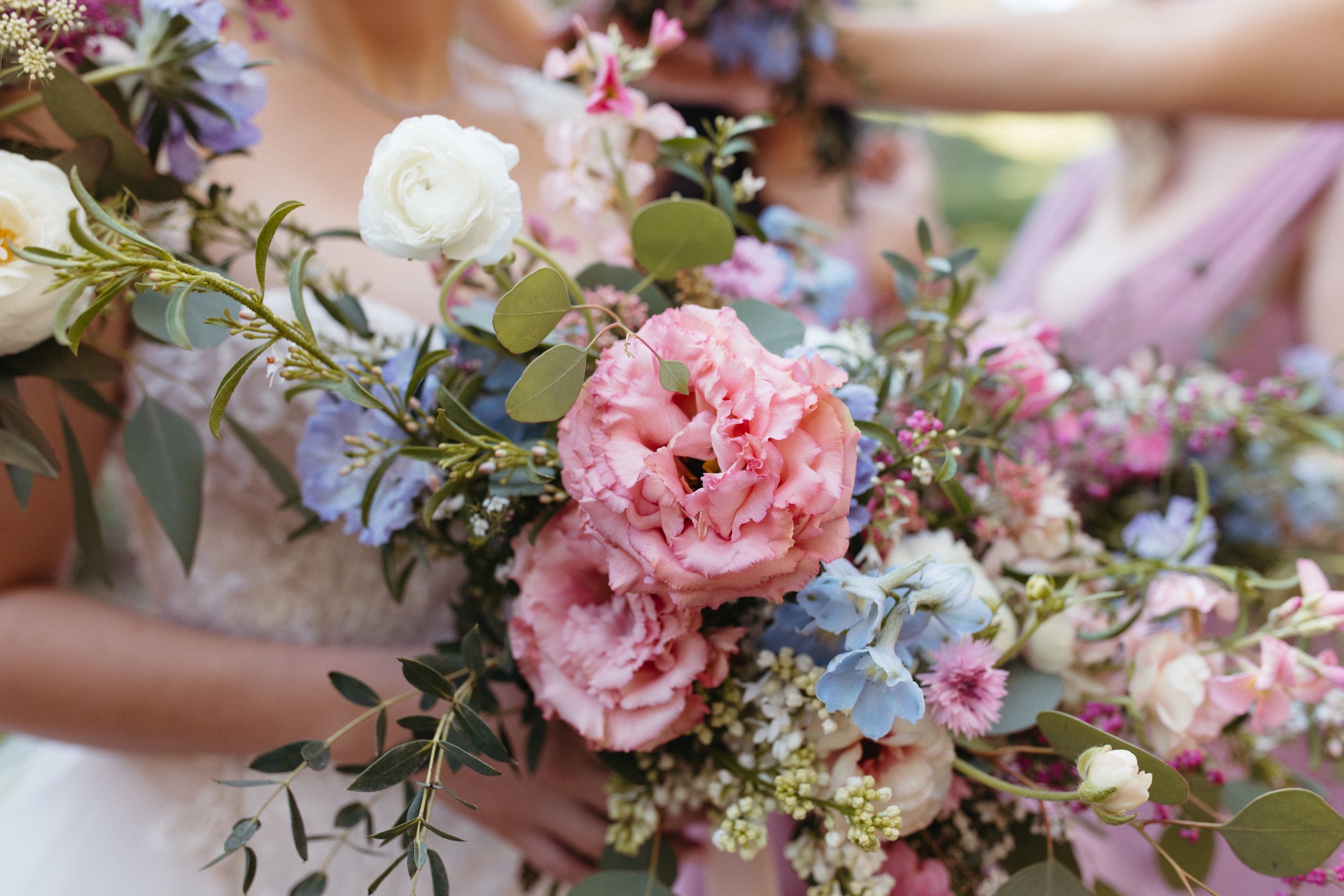 Close-up of a bride holding a large bouquet of pink, white, and blue flowers with green leaves