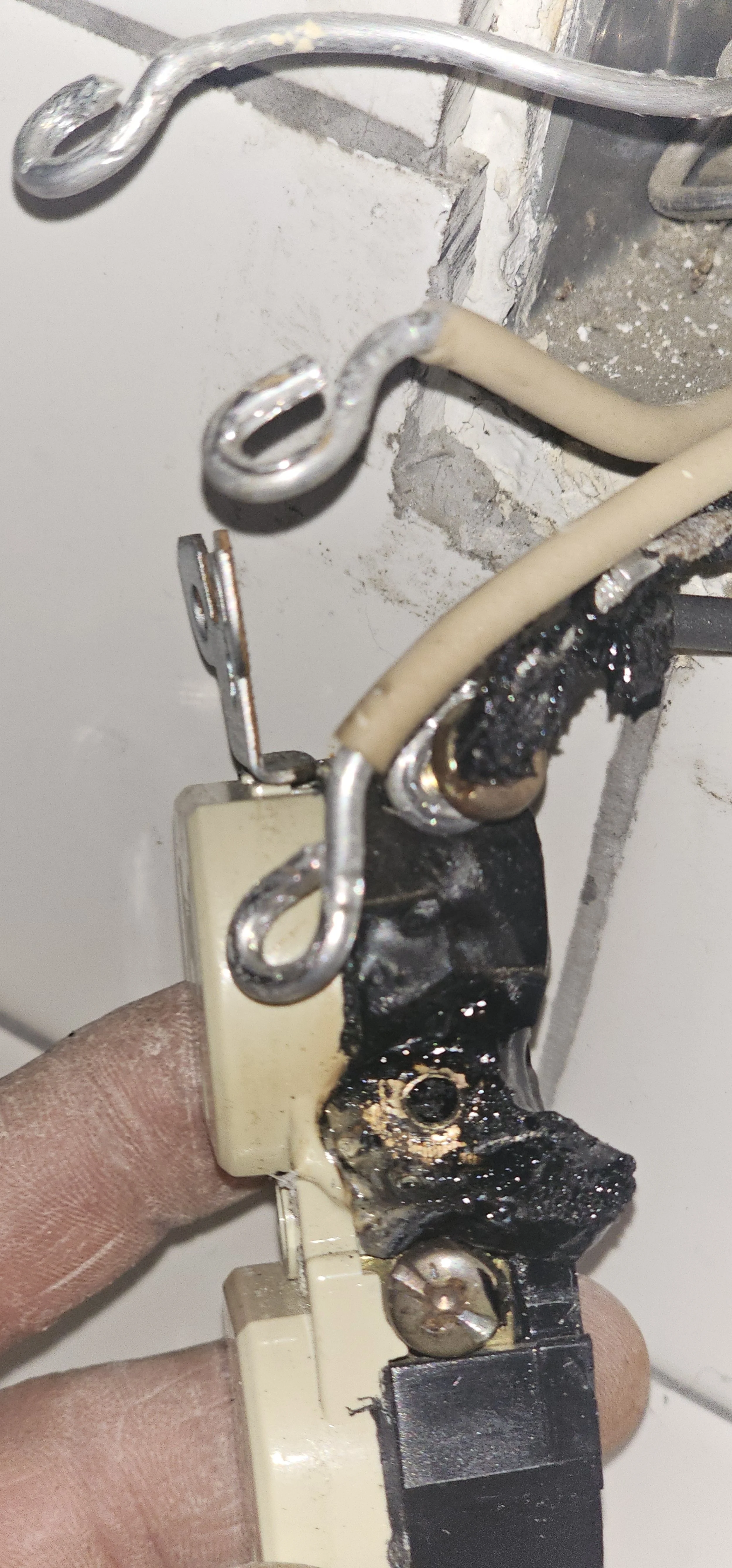 Close-up of a damaged electrical switch with burnt wiring and corroded metal parts, showing signs of fire or overheating.