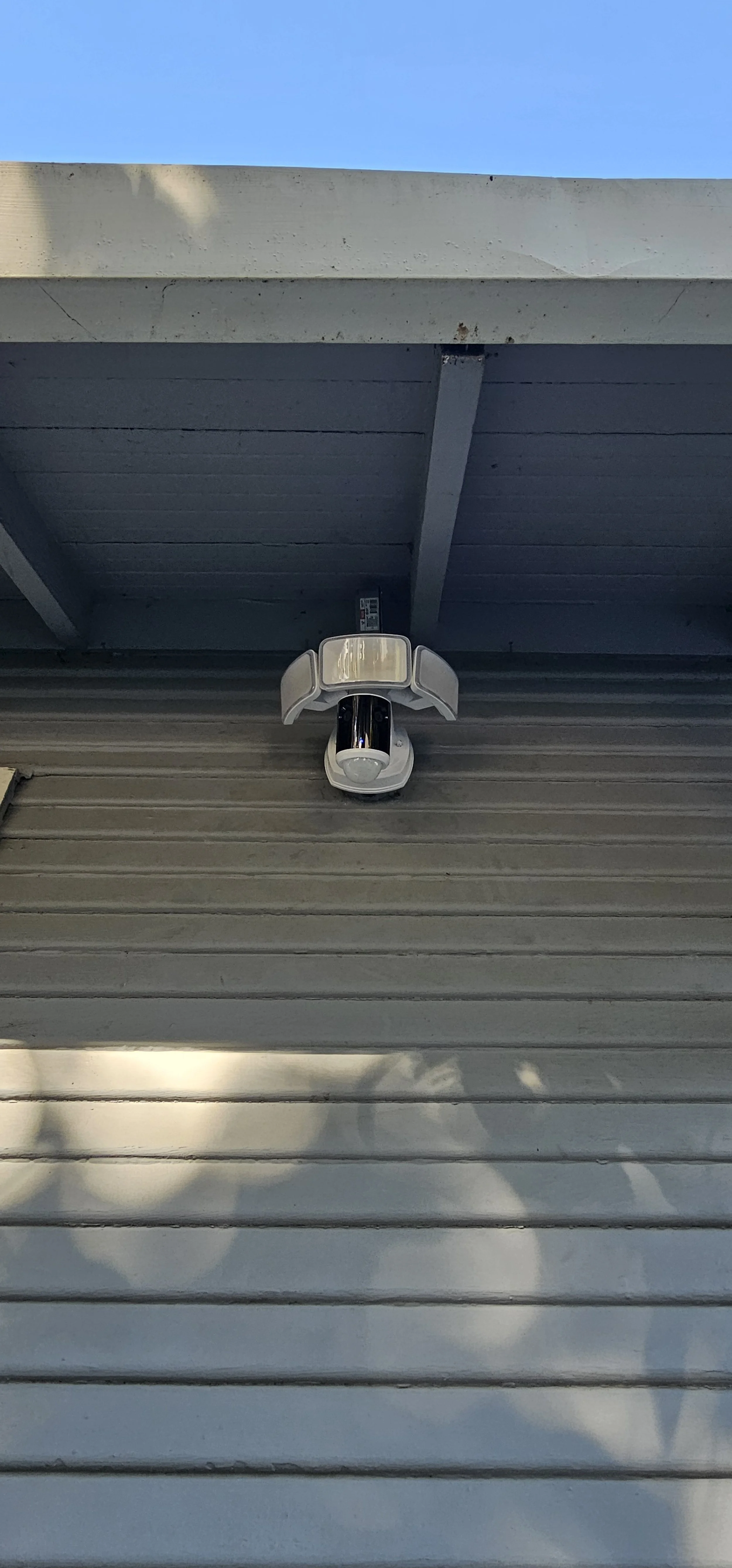 Security camera mounted on a horizontal gray metal surface under a light blue sky.