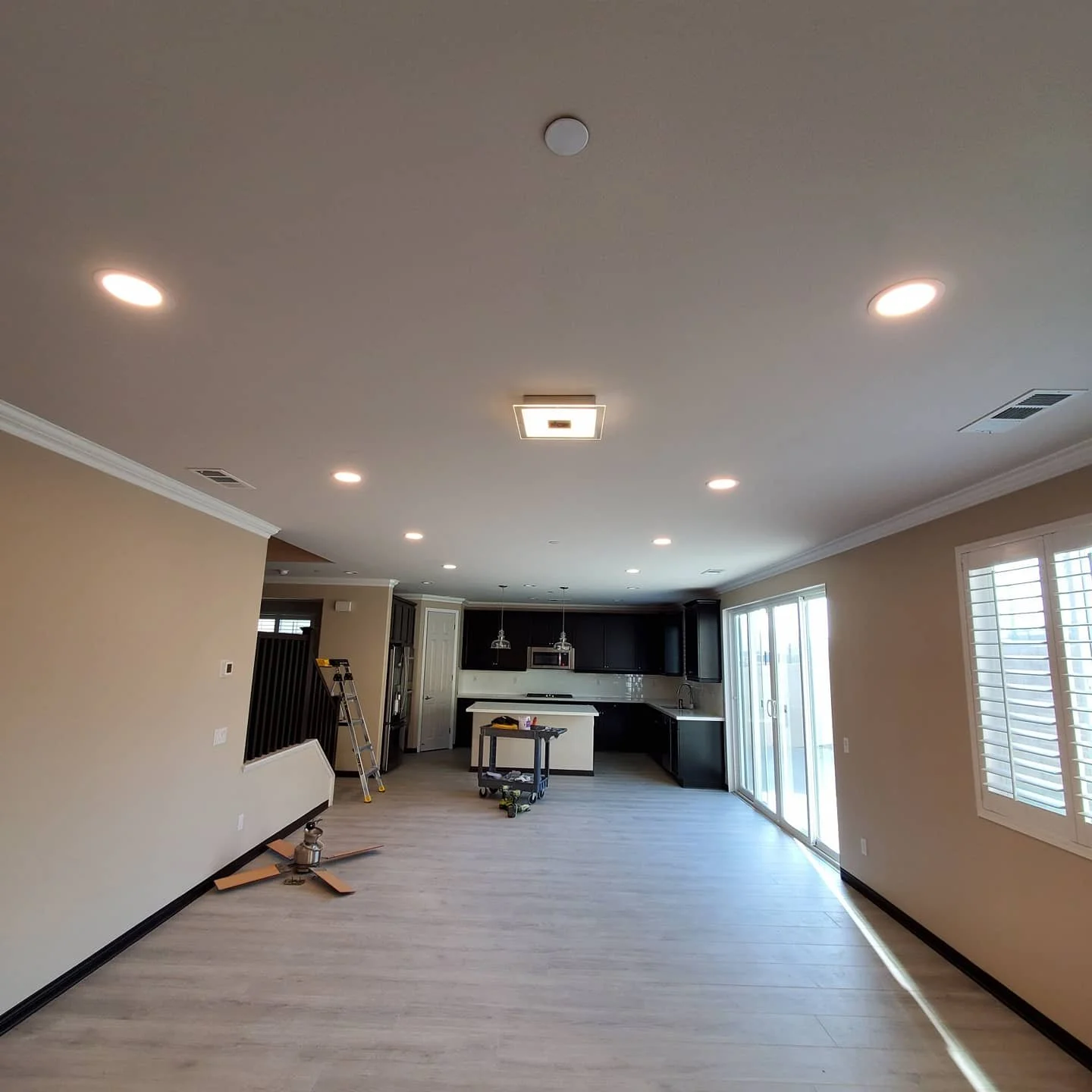 Empty living room and kitchen with recessed ceiling lights, sliding glass doors, and a ceiling fan on the floor.