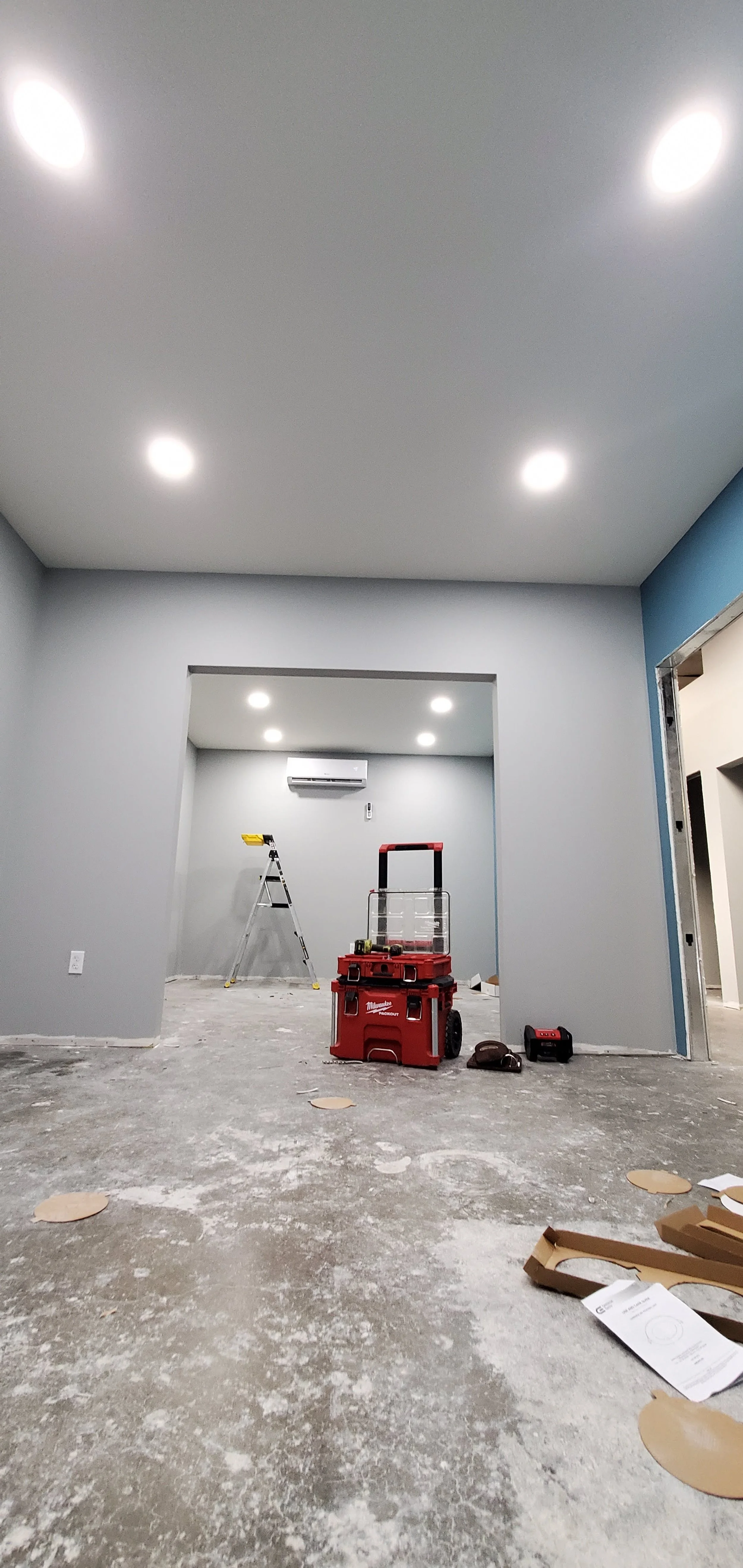 Room under renovation with a ladder, a toolbox, and construction materials on the floor, with new ceiling lights and an air conditioning unit installed.