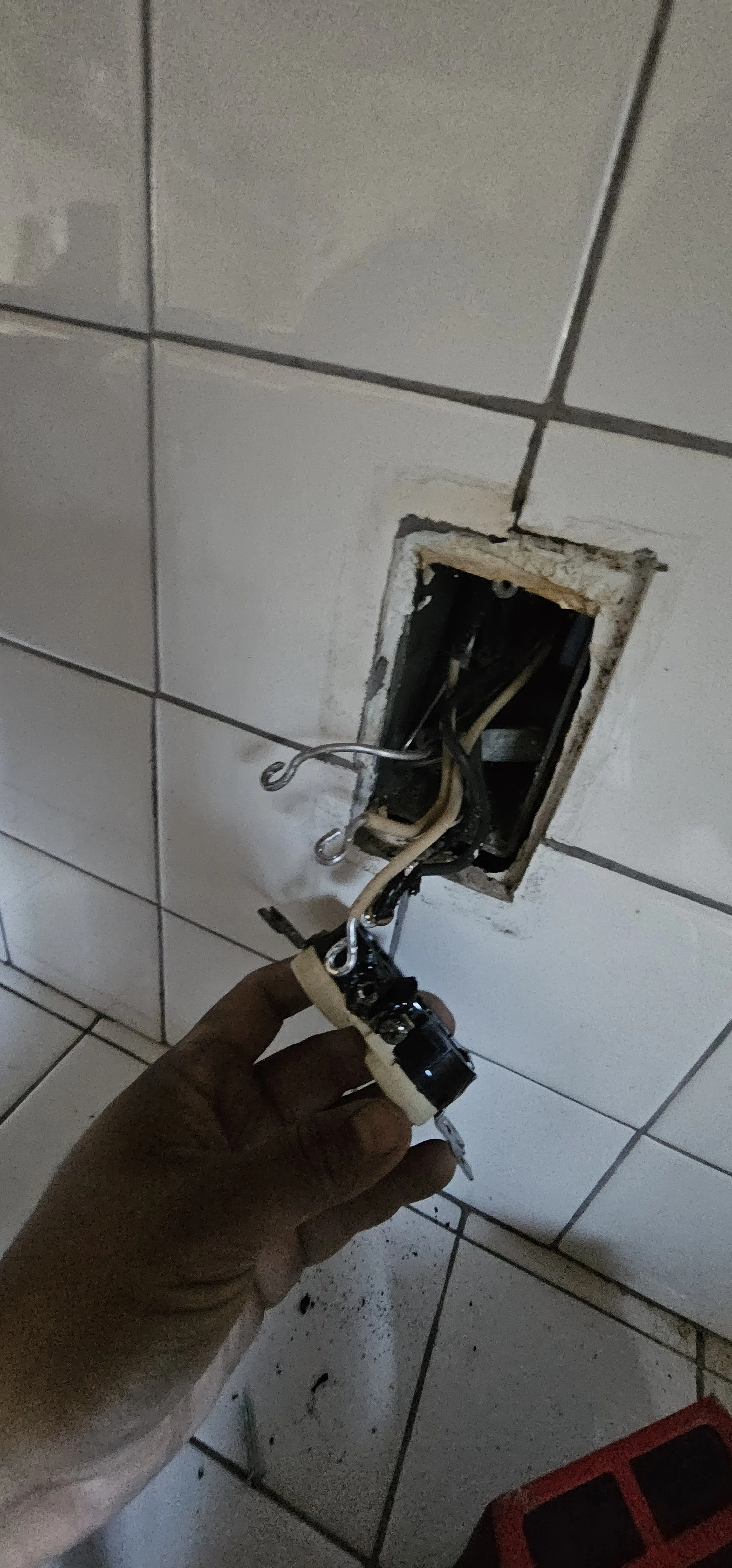 Person holding electrical wiring being installed in an open wall outlet in a tiled wall.