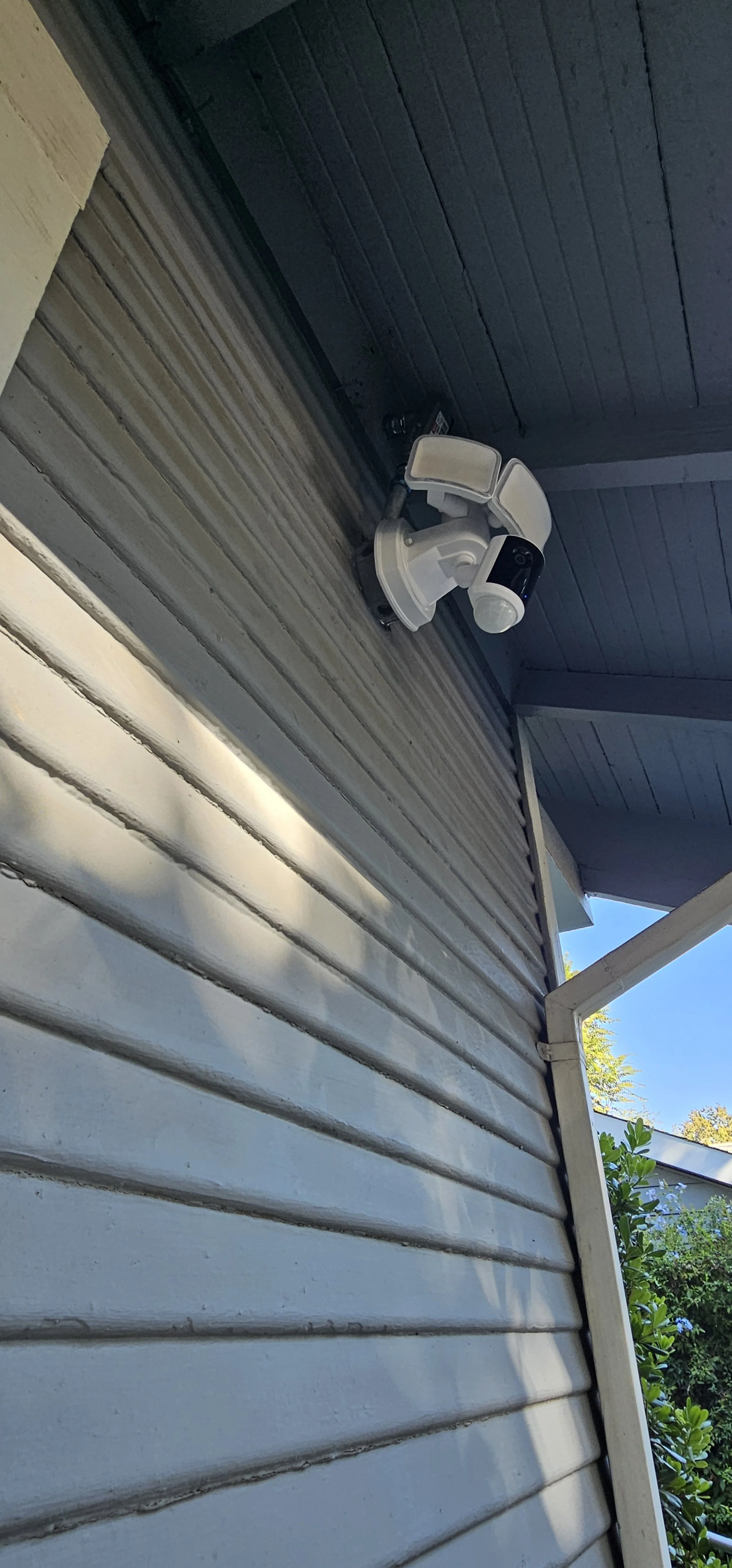 Security camera mounted on the exterior wall of a house under the porch roof.