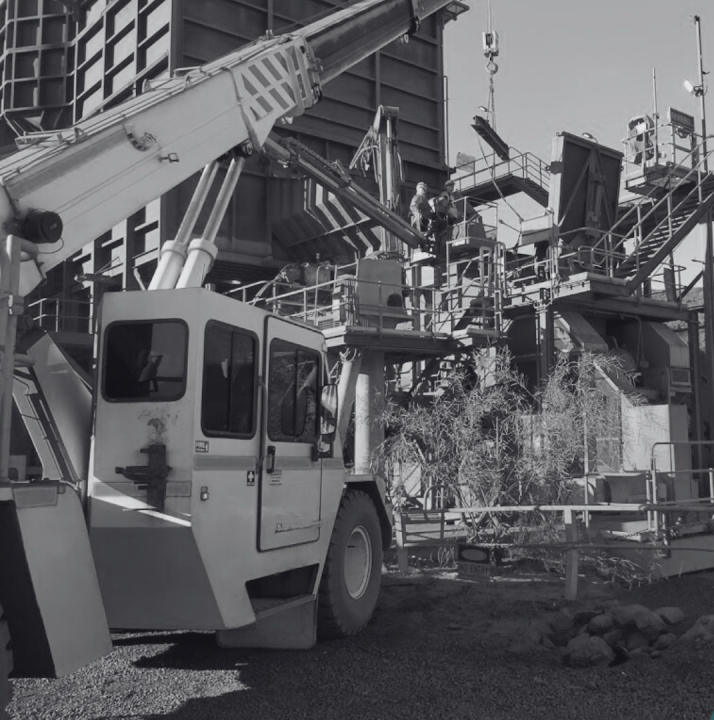 Mine site with large crane lifting materials, scaffolding, and workers wearing safety gear amid industrial structures.