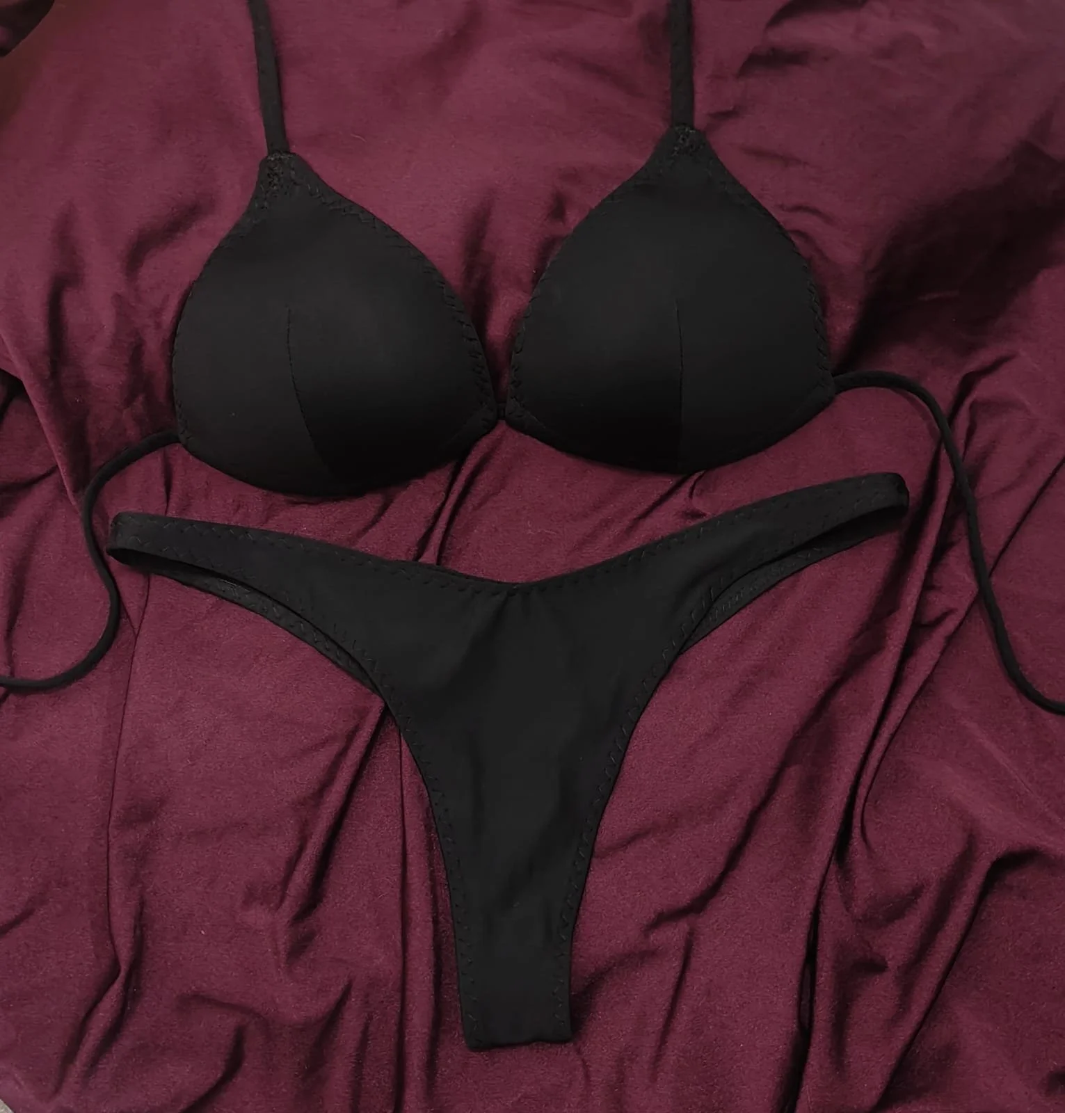 Black bikini top and bottom on a maroon fabric background.